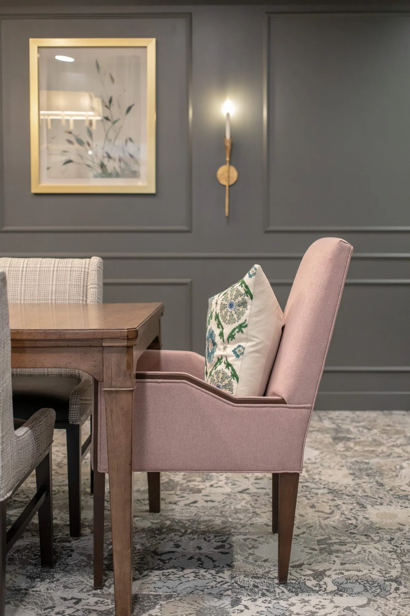 Active adult community interior detail: pink upholstered armchair with a floral pillow at a wood table by grey panelling