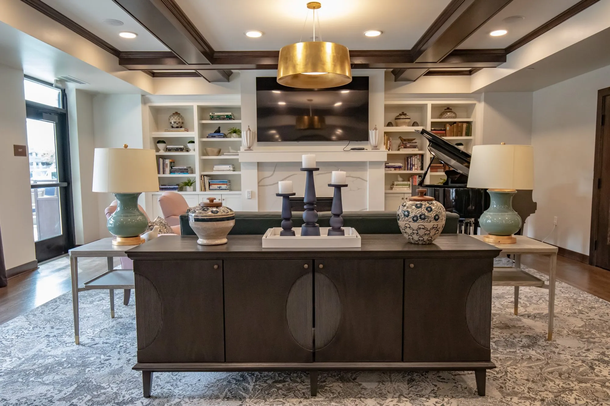 Active adult community living room with blue ceramic lamps on a console before a fireplace wall with shelving and a piano