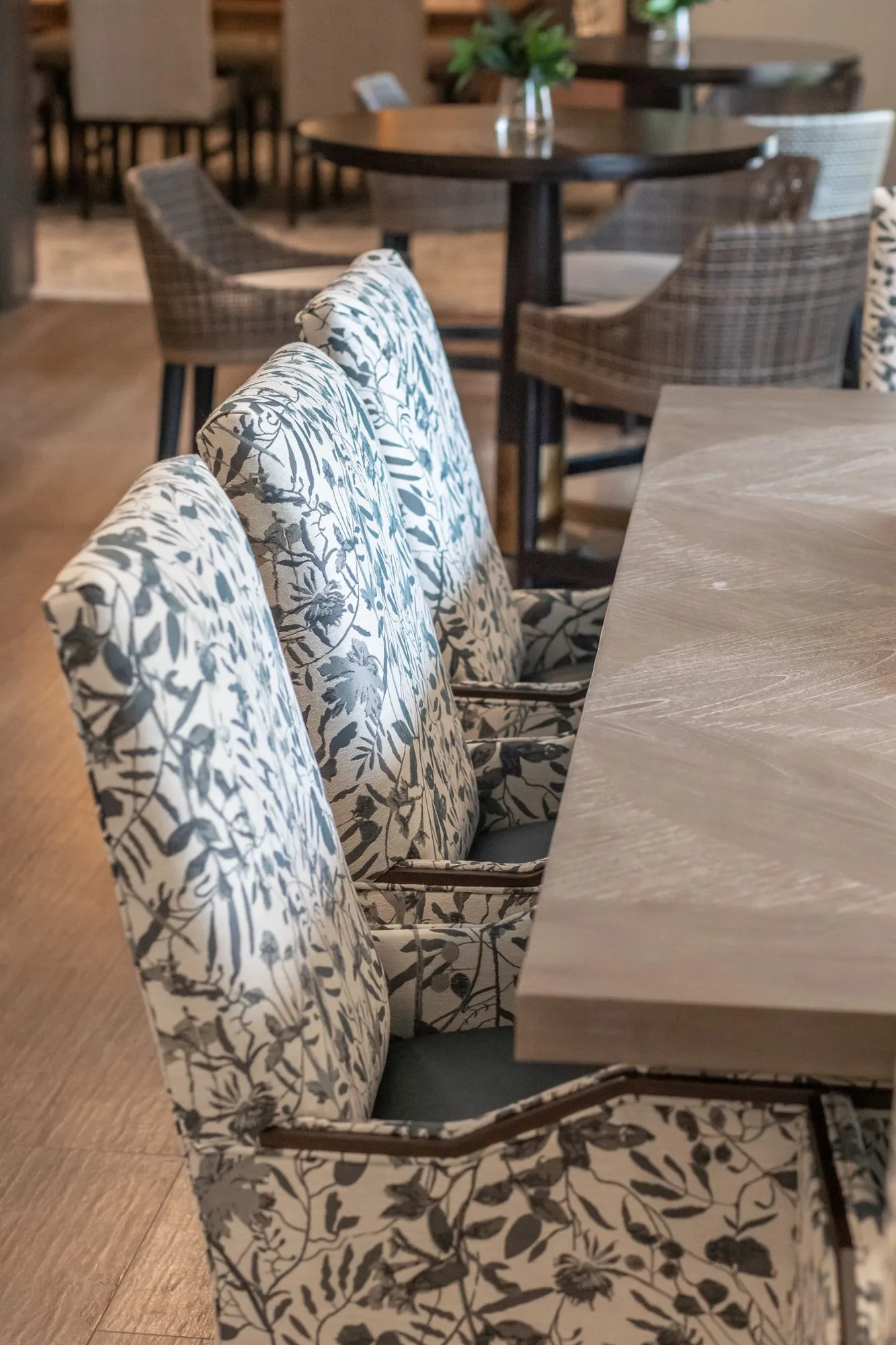 Active adult community interior detail: grey and white botanical print chairs lined along a wood dining table