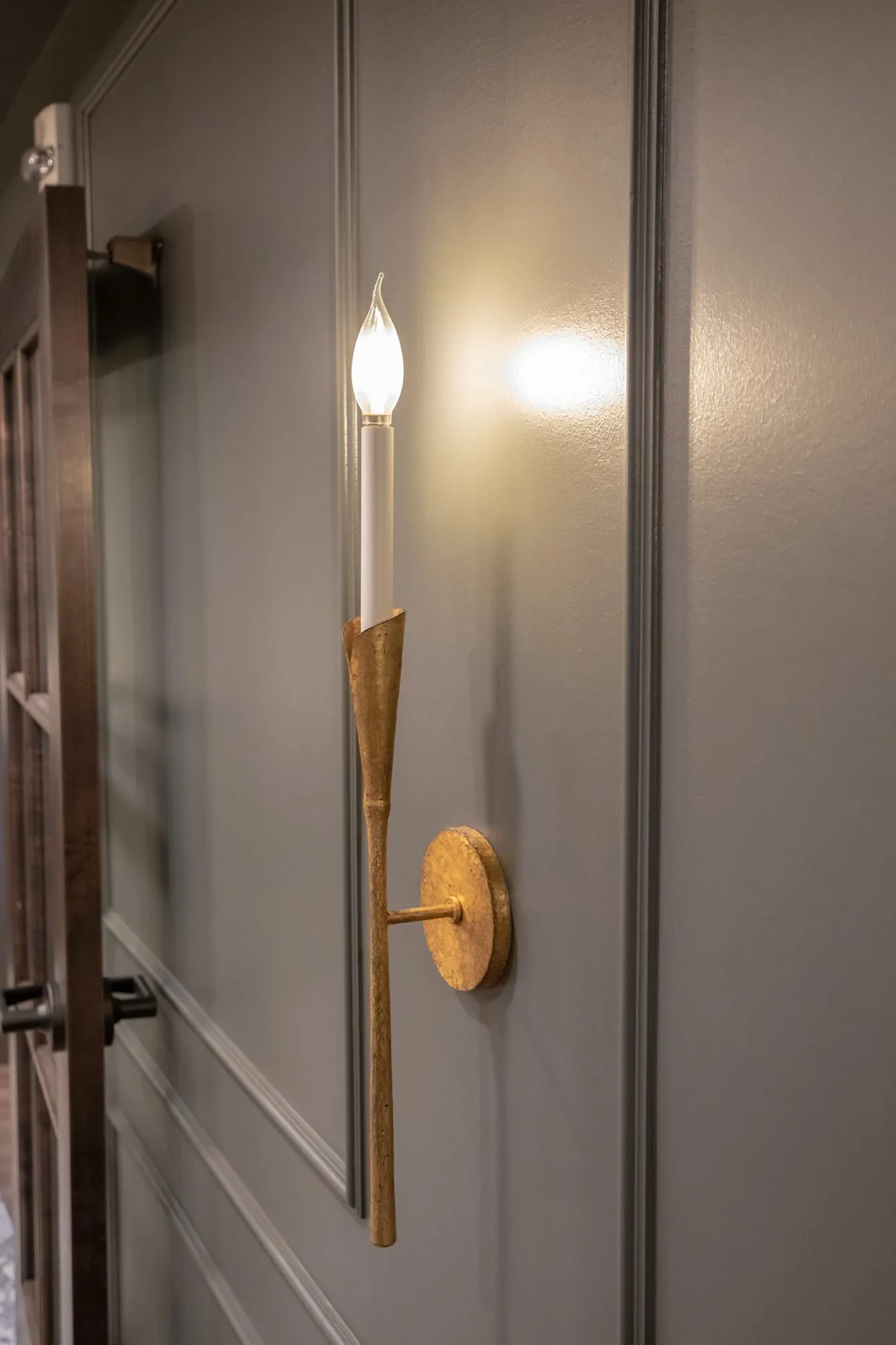 Active adult community interior detail: gold torch sconce with a candle bulb on a grey panelled wall