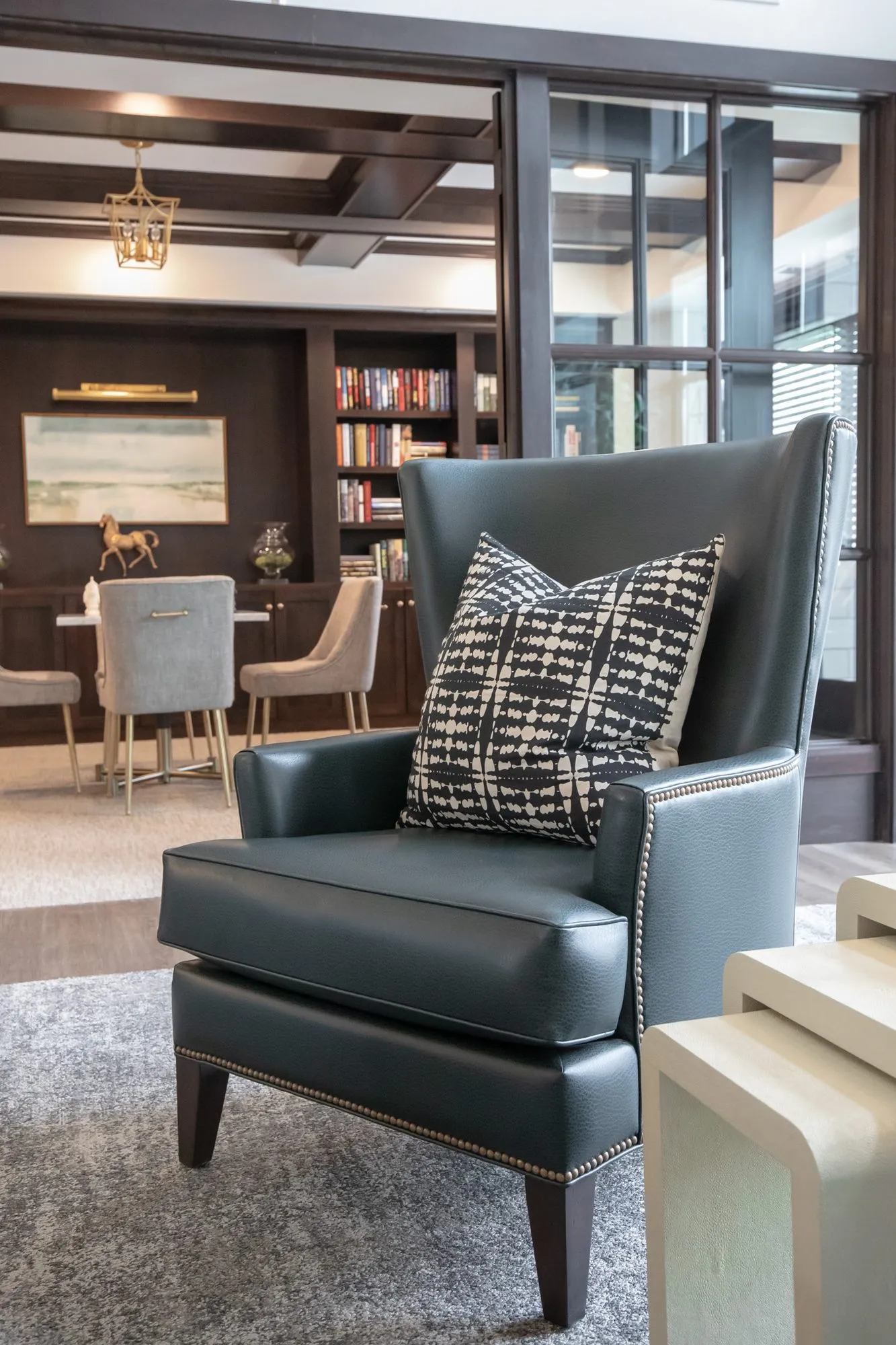 Active adult community interior detail: teal leather wingback chair, the library and its bookcases behind glass doors