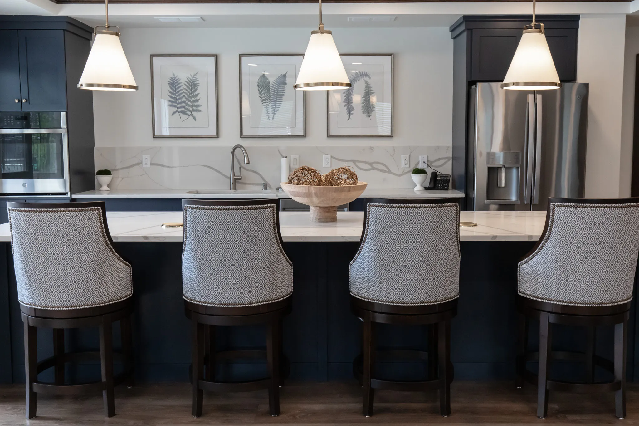 Active adult community club kitchen with navy cabinetry and a quartz island, patterned stools under white pendants