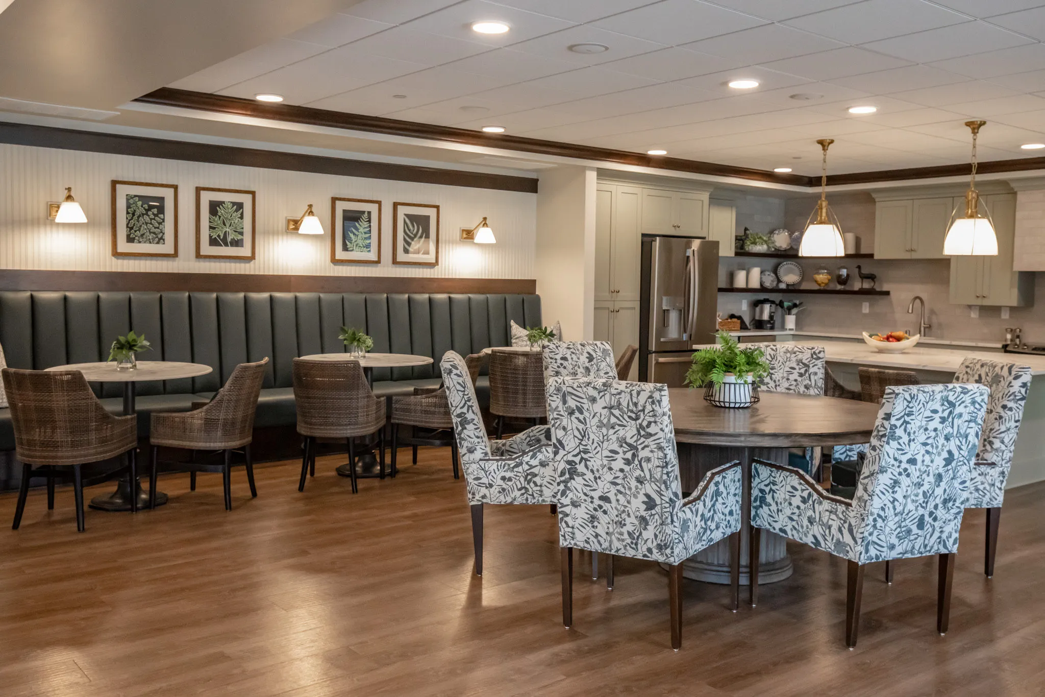 Active adult community coffee lounge with a green leather banquette, woven chairs and floral wing chairs at a round table