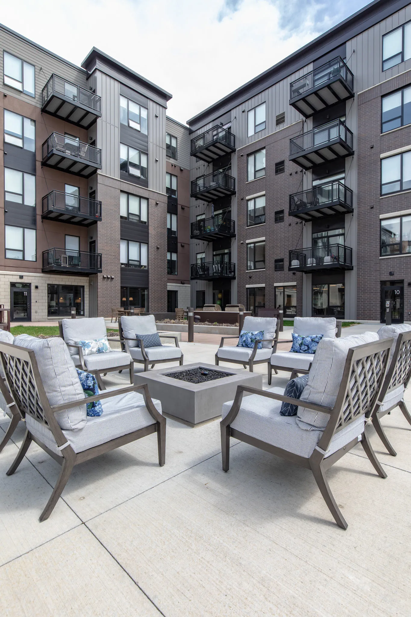 Active adult community courtyard with cushioned lattice-back chairs around a concrete fire table, apartment balconies behind