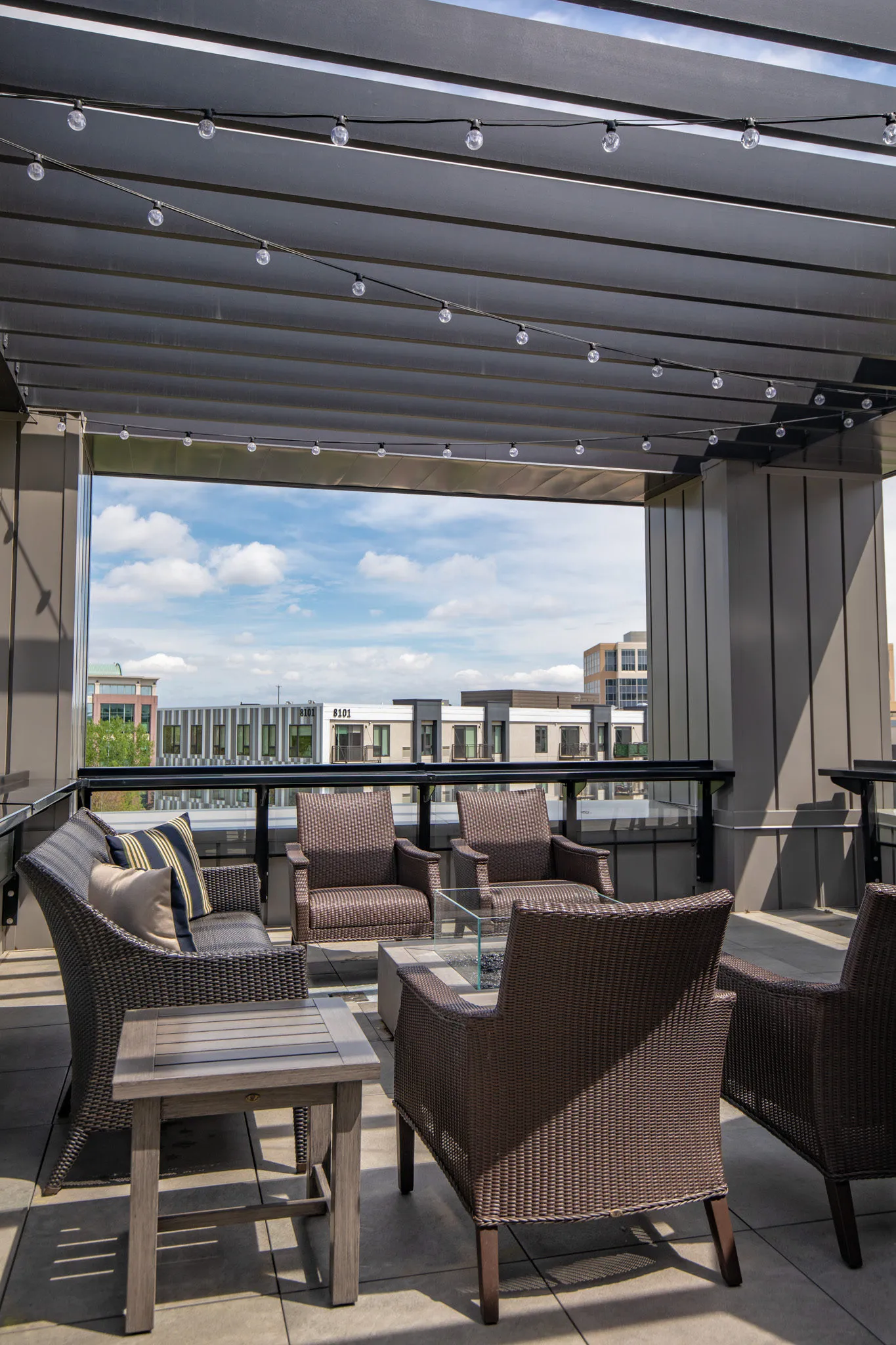 Active adult community covered patio with string lights under the pergola above woven armchairs and a low table