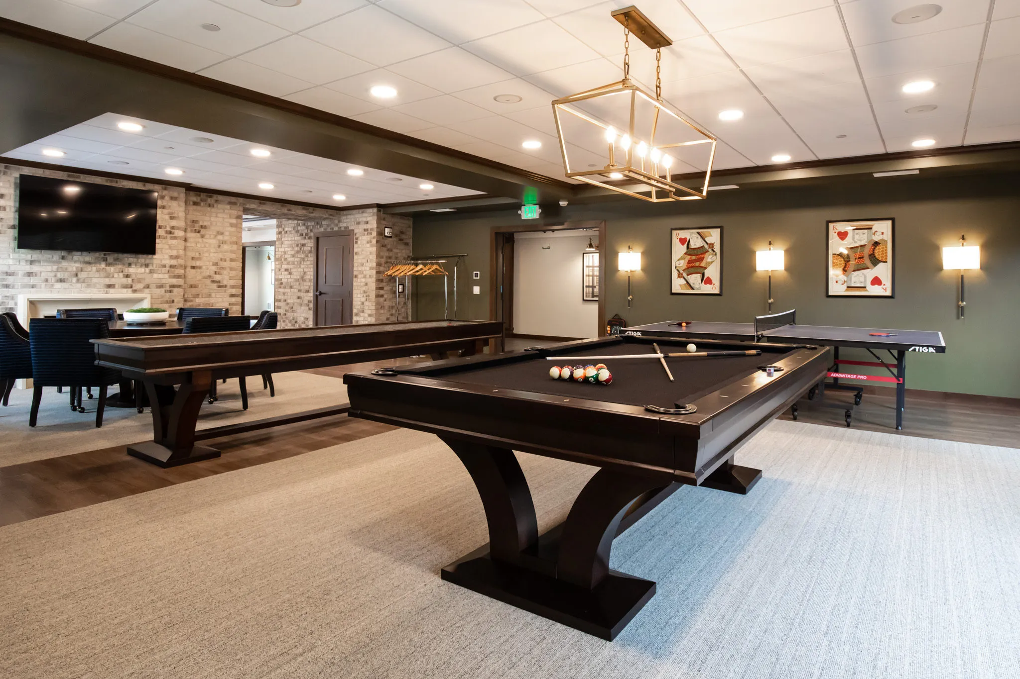 Active adult community game room with a billiards table and table tennis under a brass lantern, a brick chimney beyond