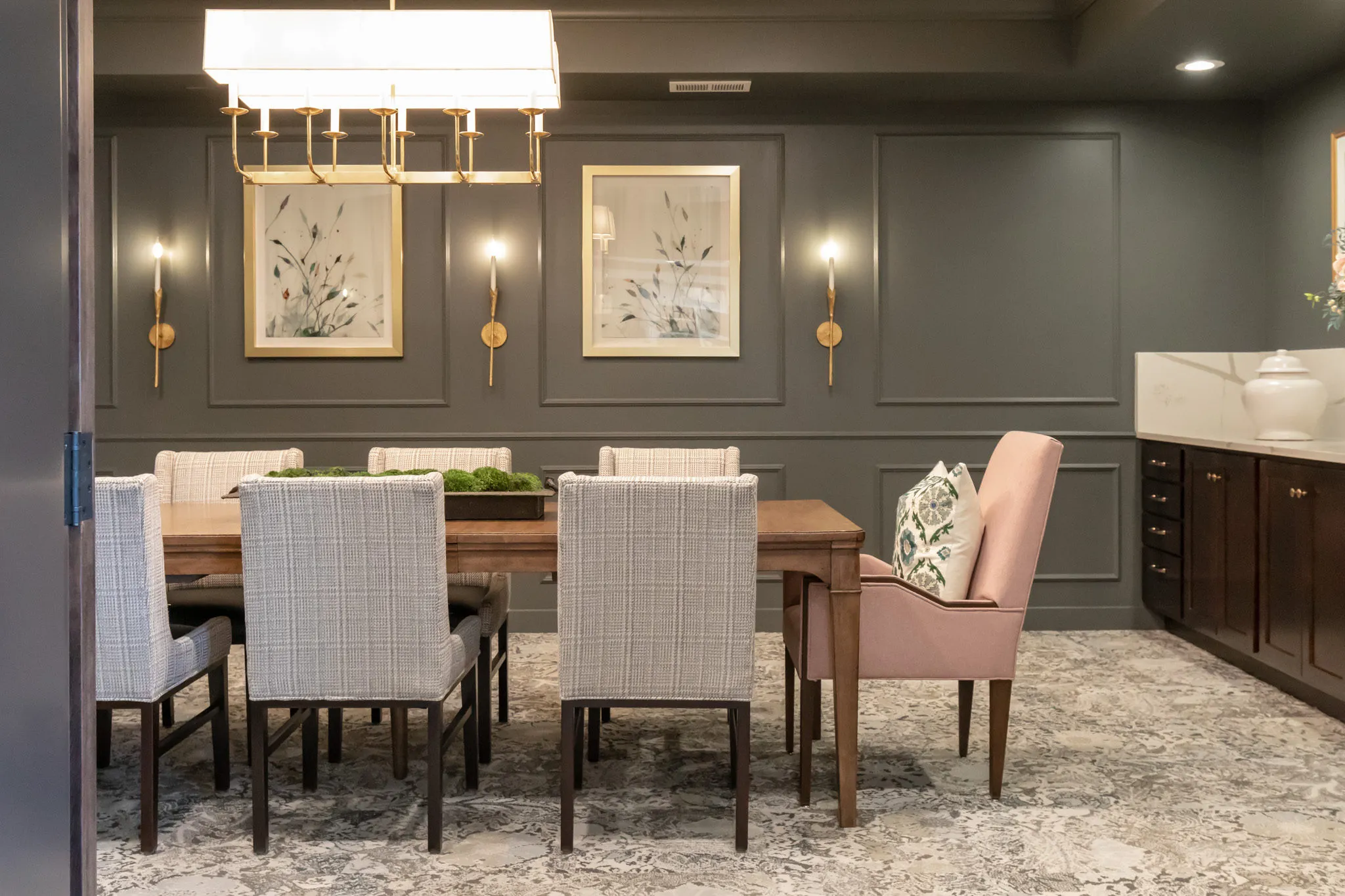 Active adult community private dining room with olive panelled walls and a brass linear chandelier above a walnut table