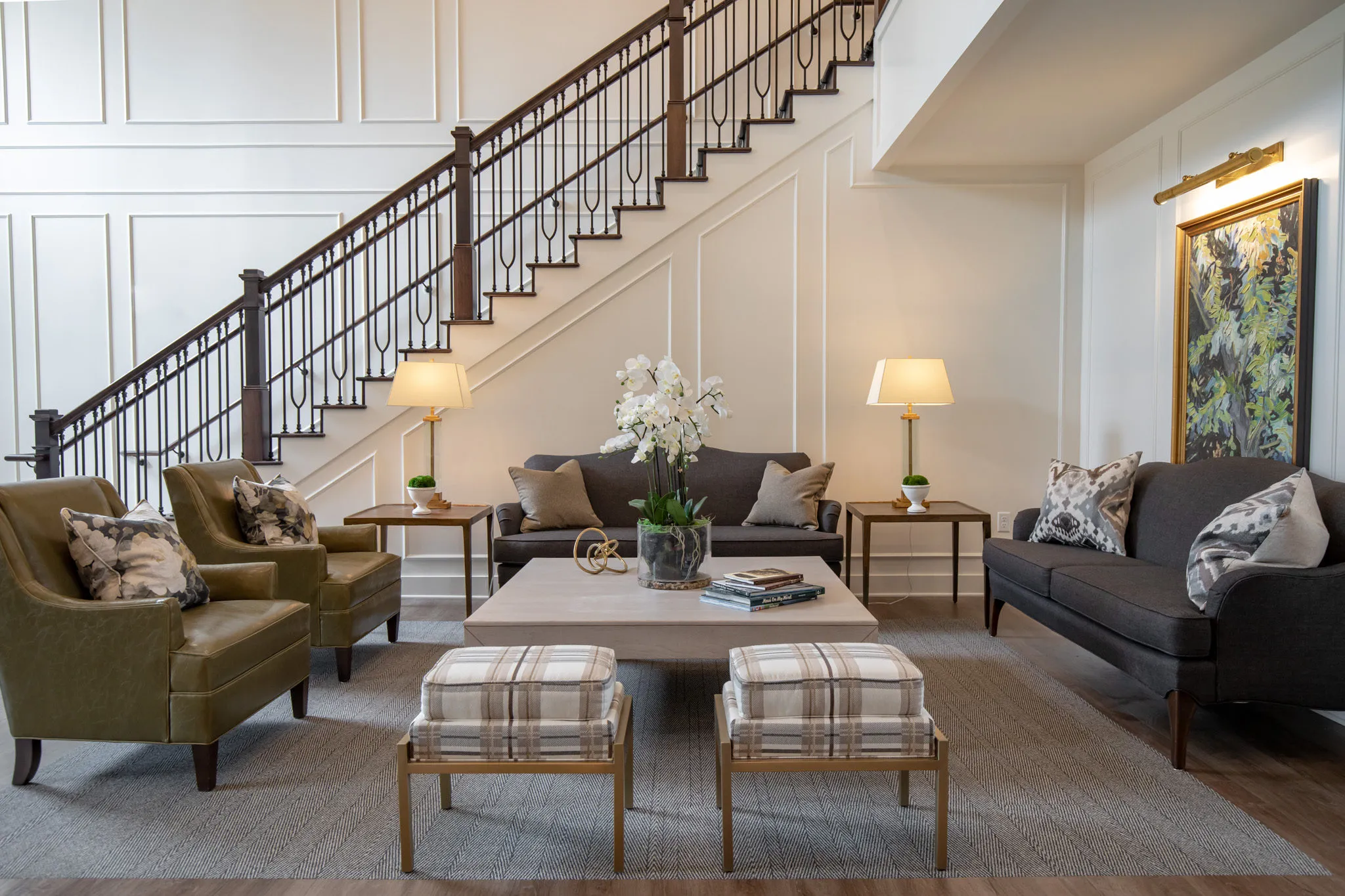 Active adult community living room with olive club chairs and plaid benches on a sisal rug below the open stair