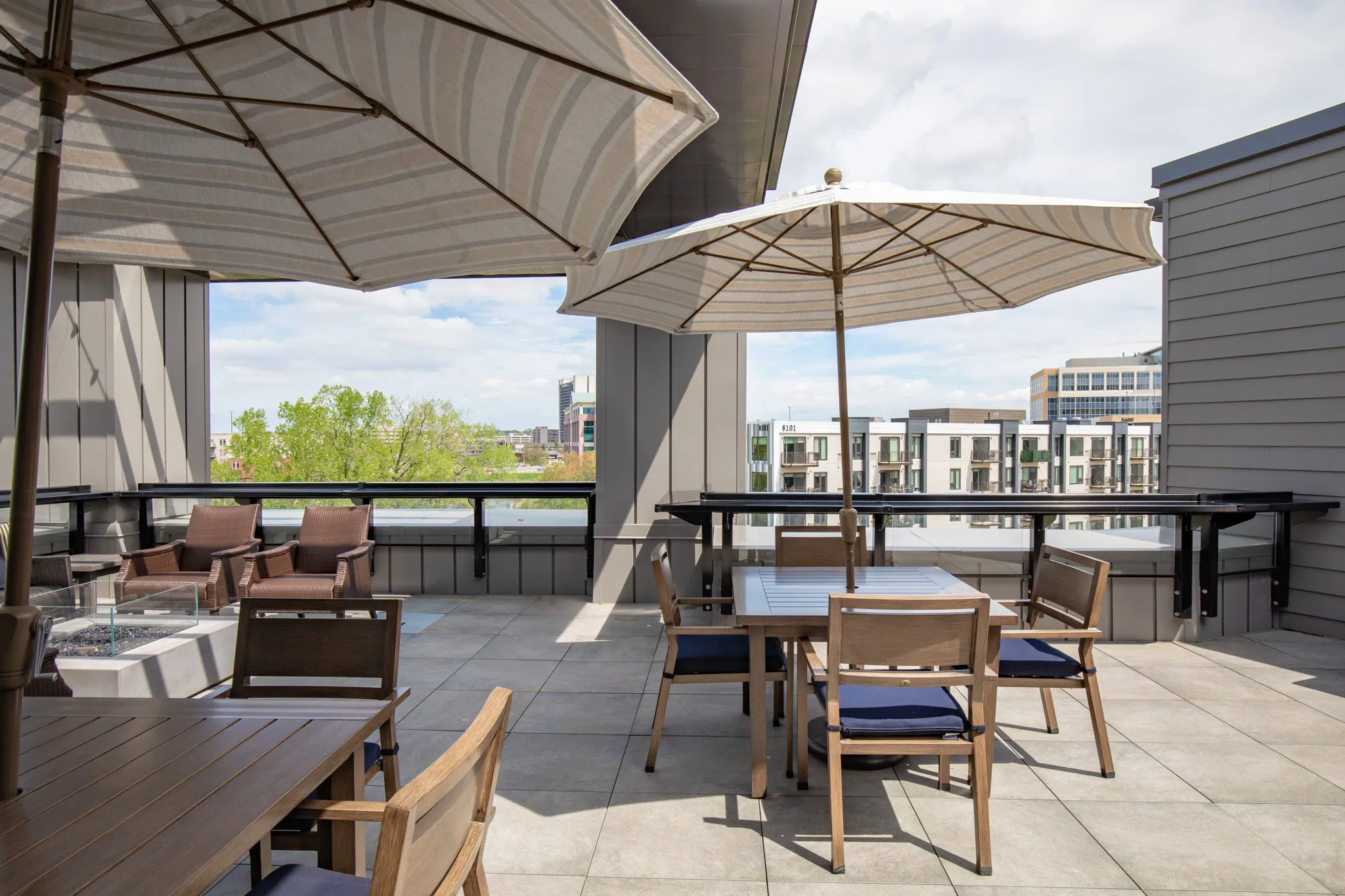 Active adult community terrace with market umbrellas over teak dining tables looking out to the treeline