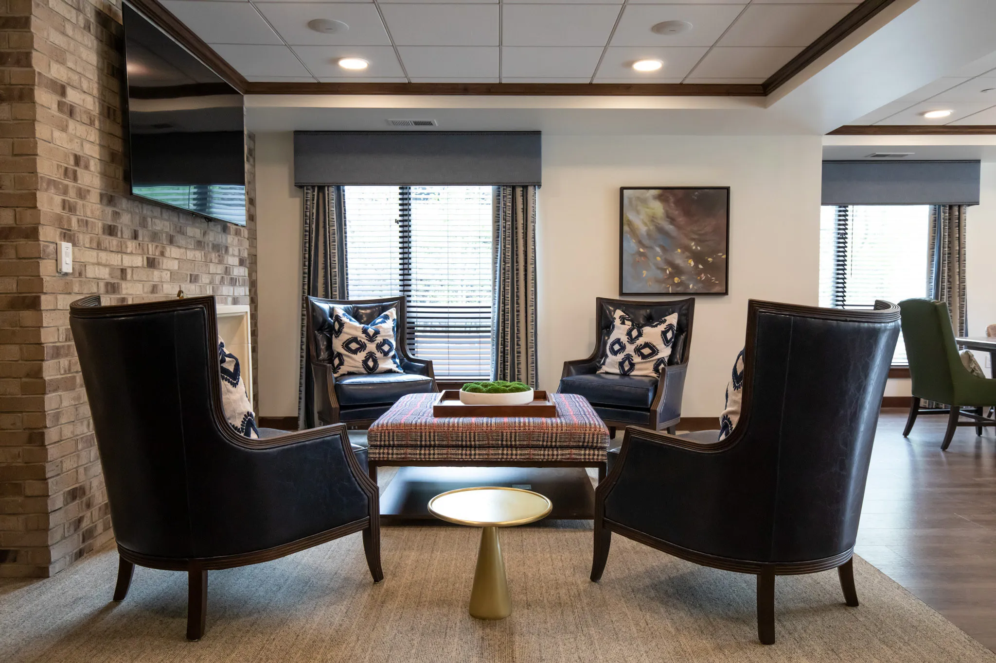 Active adult community television lounge with black leather wing chairs and ikat pillows facing a brick pier