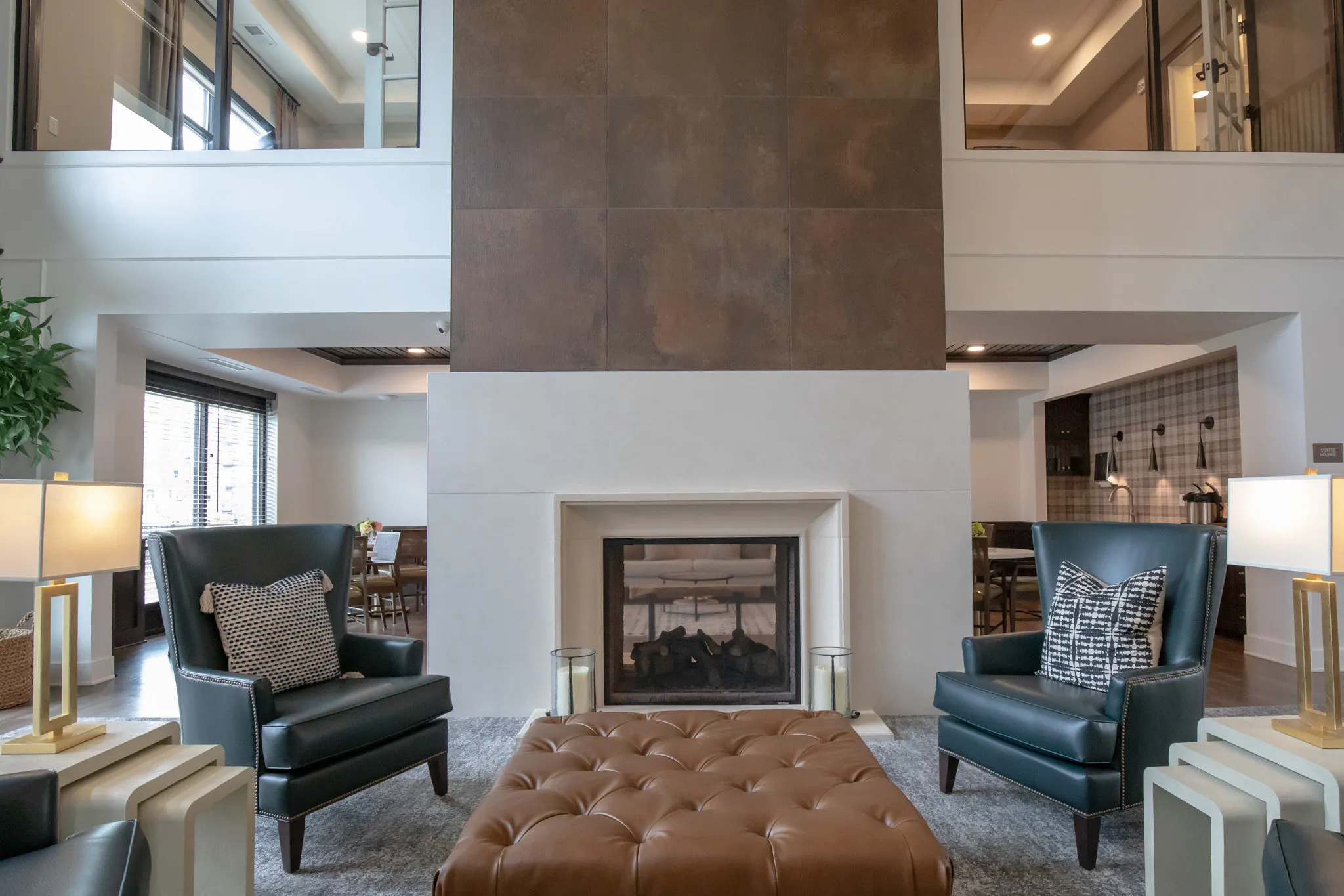 Active adult community two-story lounge, a bronze tile fireplace surround between teal leather wingbacks and a tan ottoman