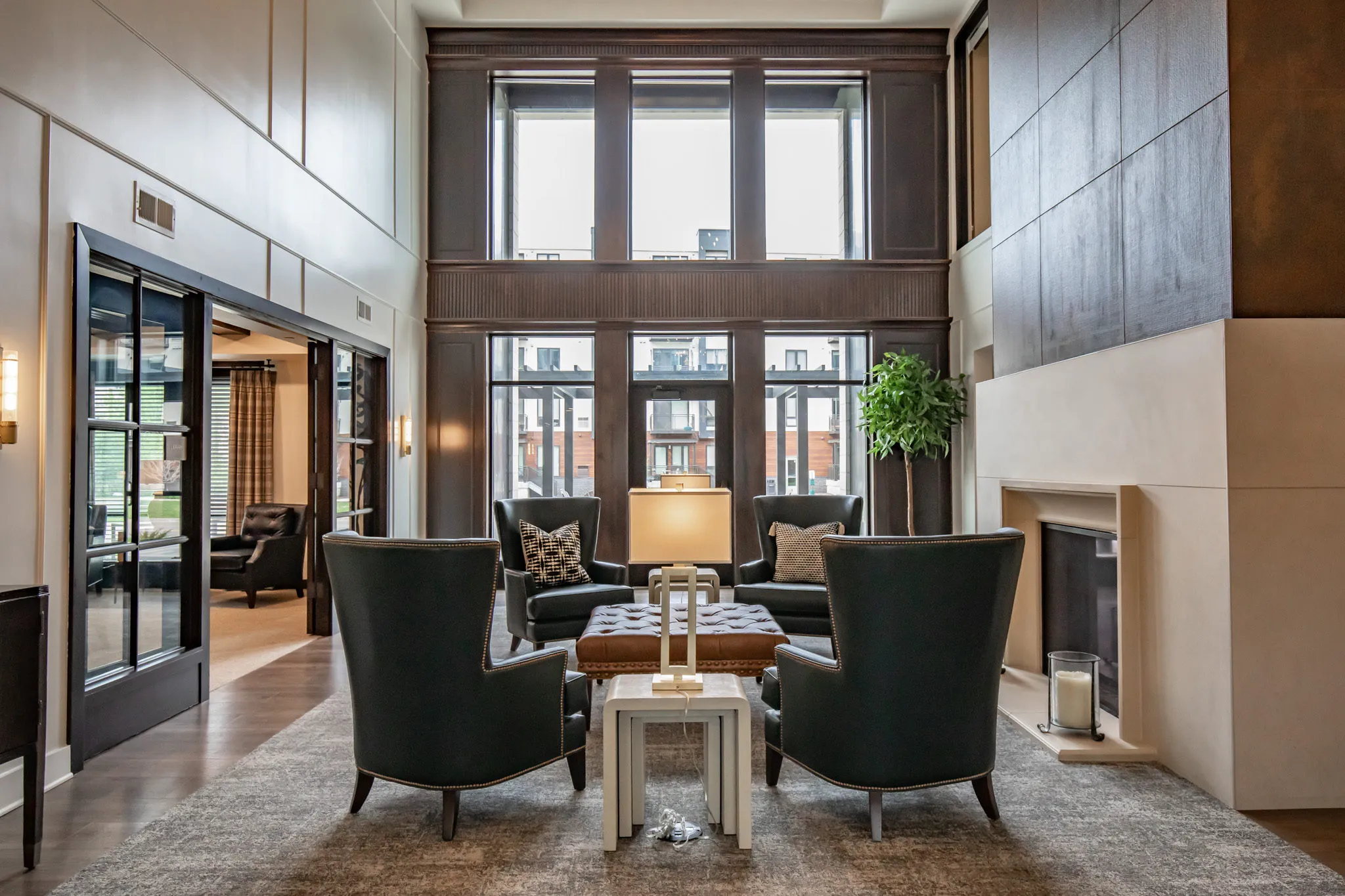 Active adult community two-story lobby with a dark wood window wall above green wingback chairs around a tufted ottoman