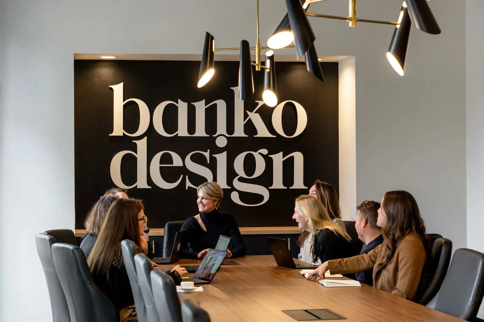 Banko Design team members in conversation around the conference table beneath the studio's black wordmark wall
