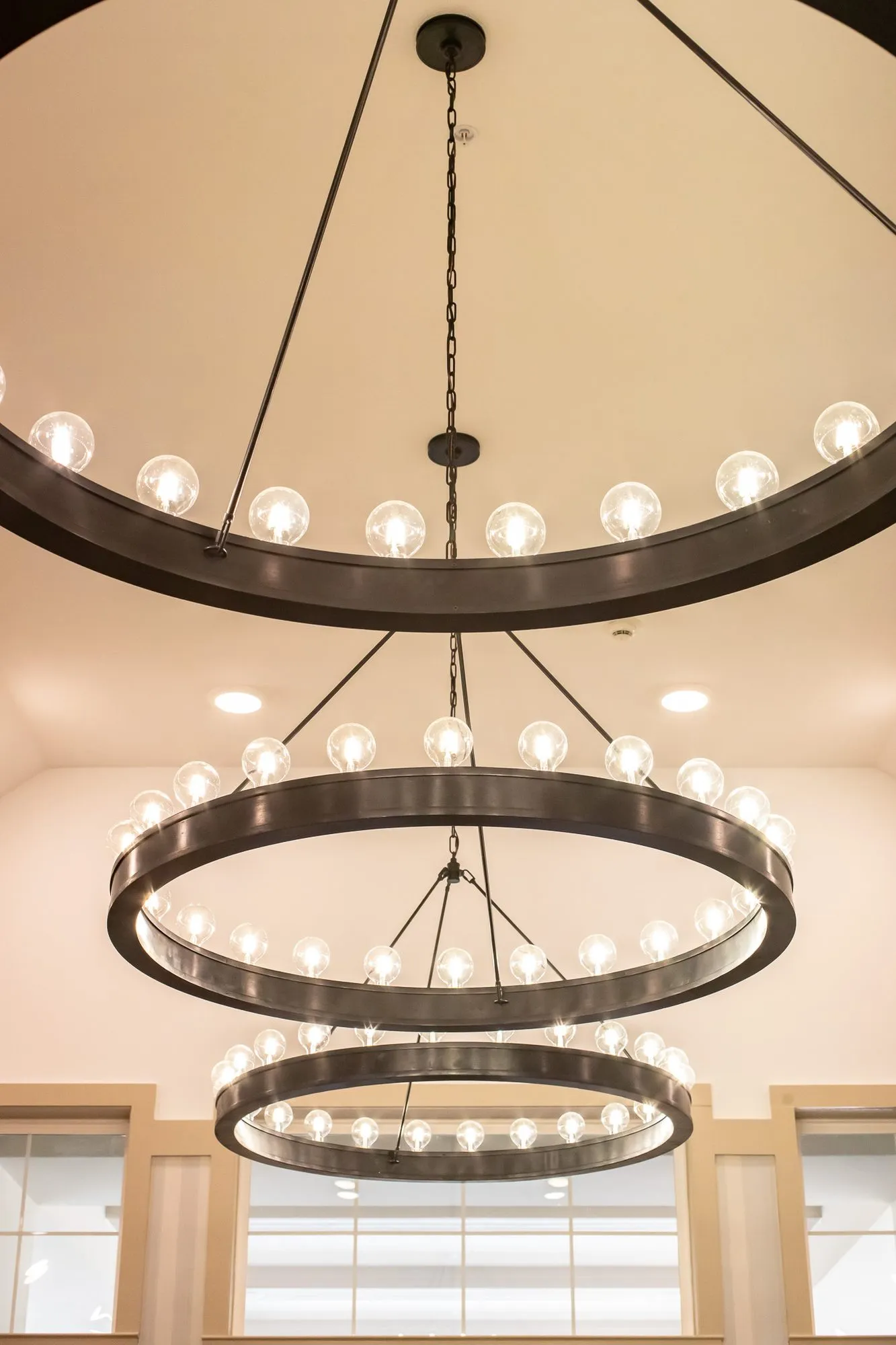 Senior living interior detail: three tiers of black iron ring chandeliers with globe bulbs, interior design by Banko Design at The Blake At Tyler, Tyler, Texas