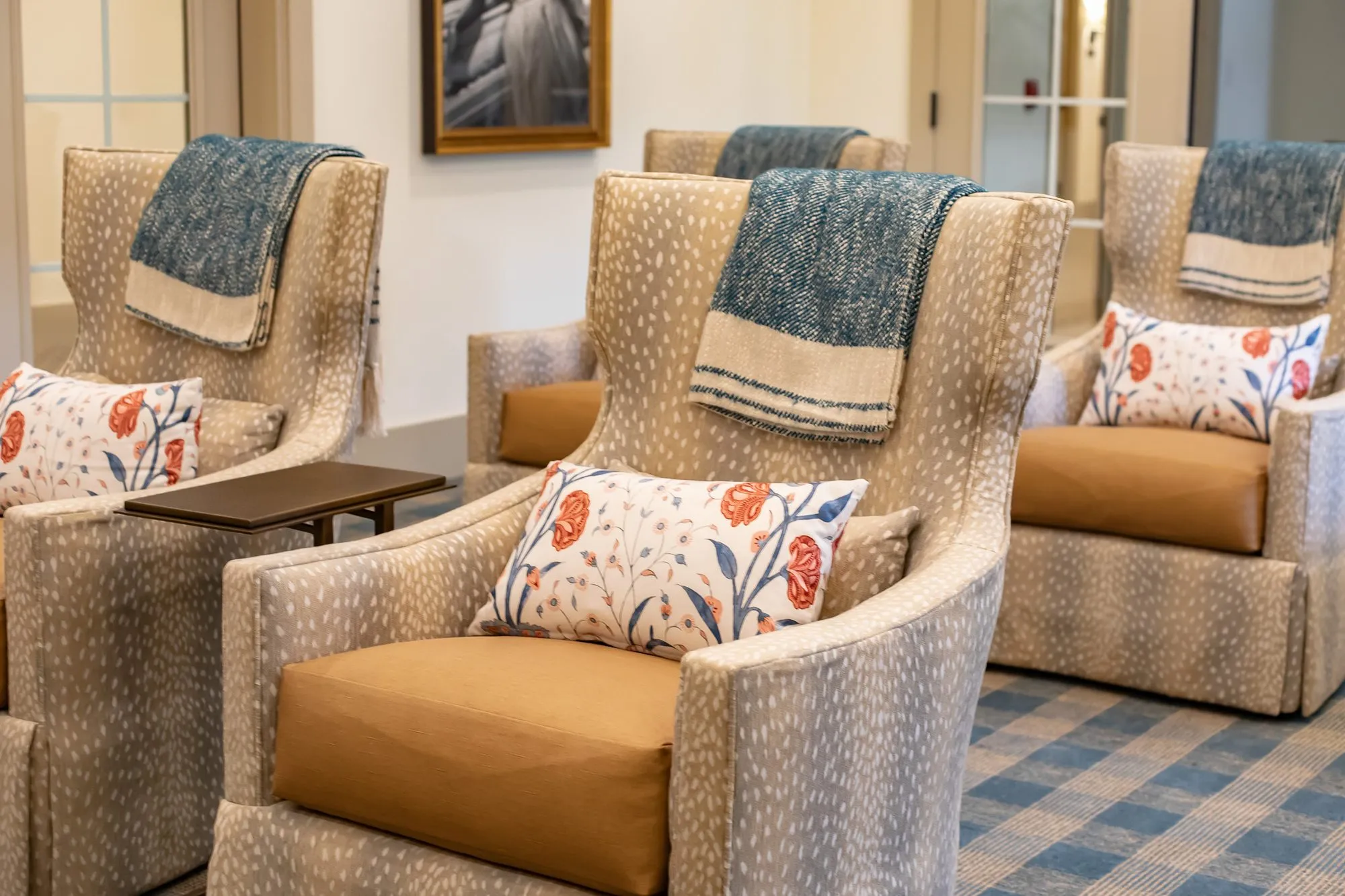 Senior living interior detail: fawn print wingback recliners with cognac leather seats, floral pillows and blue throws