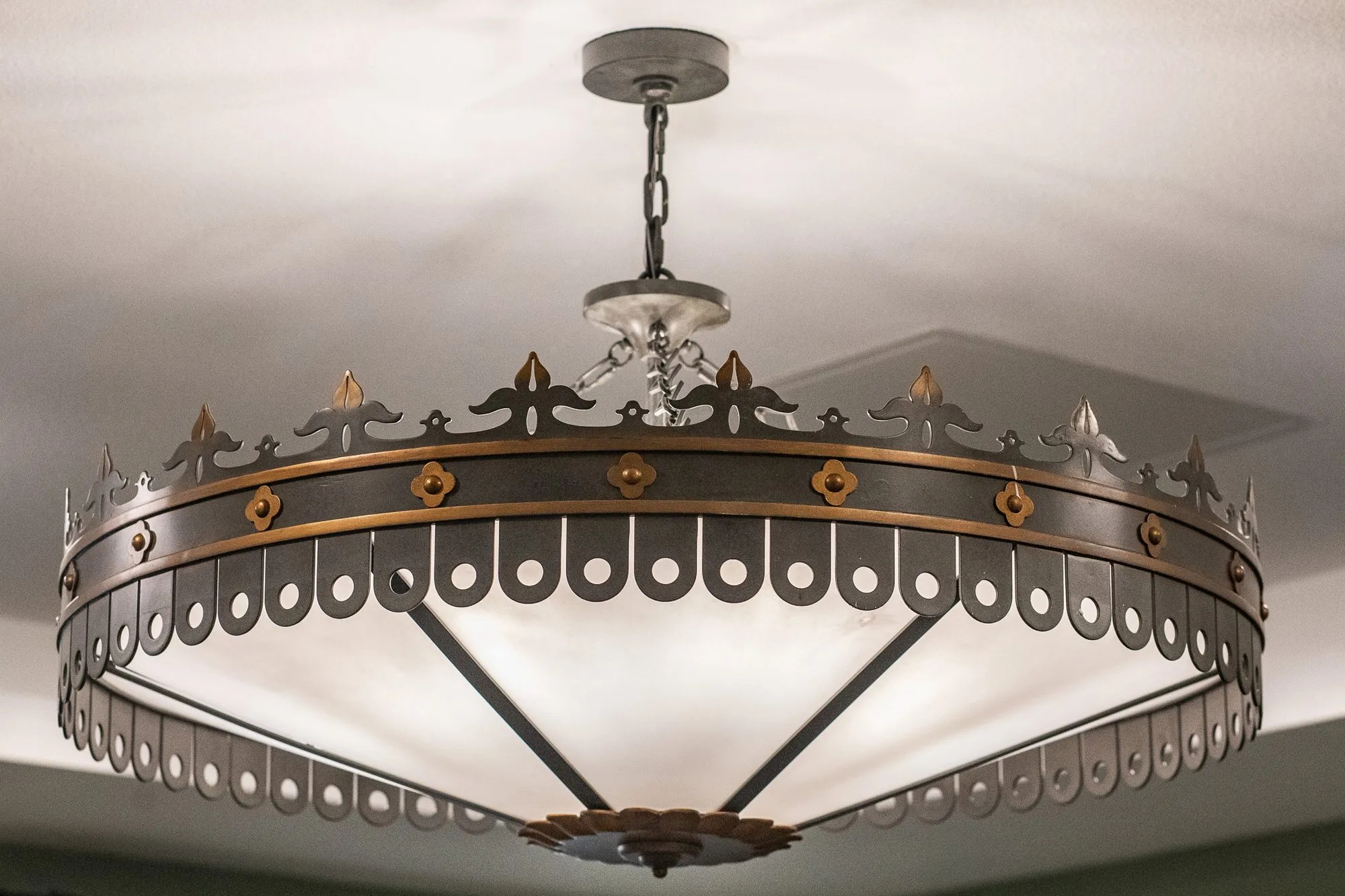 Senior living interior detail: bronze ceiling fixture with a pierced crown shaped band around a white glass bowl