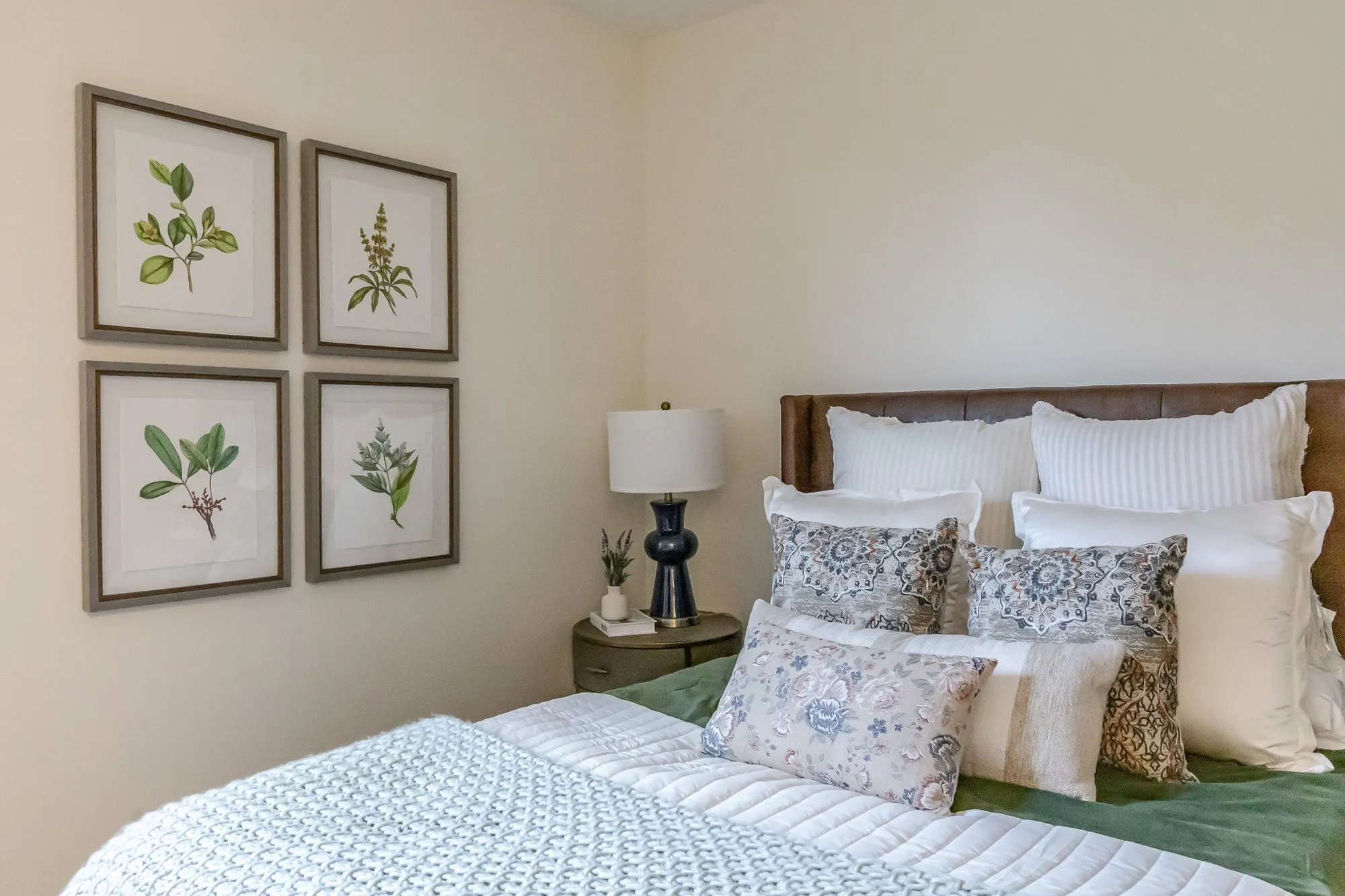 Senior living model bedroom with a leather headboard, blue and white patterned pillows and four framed botanical prints