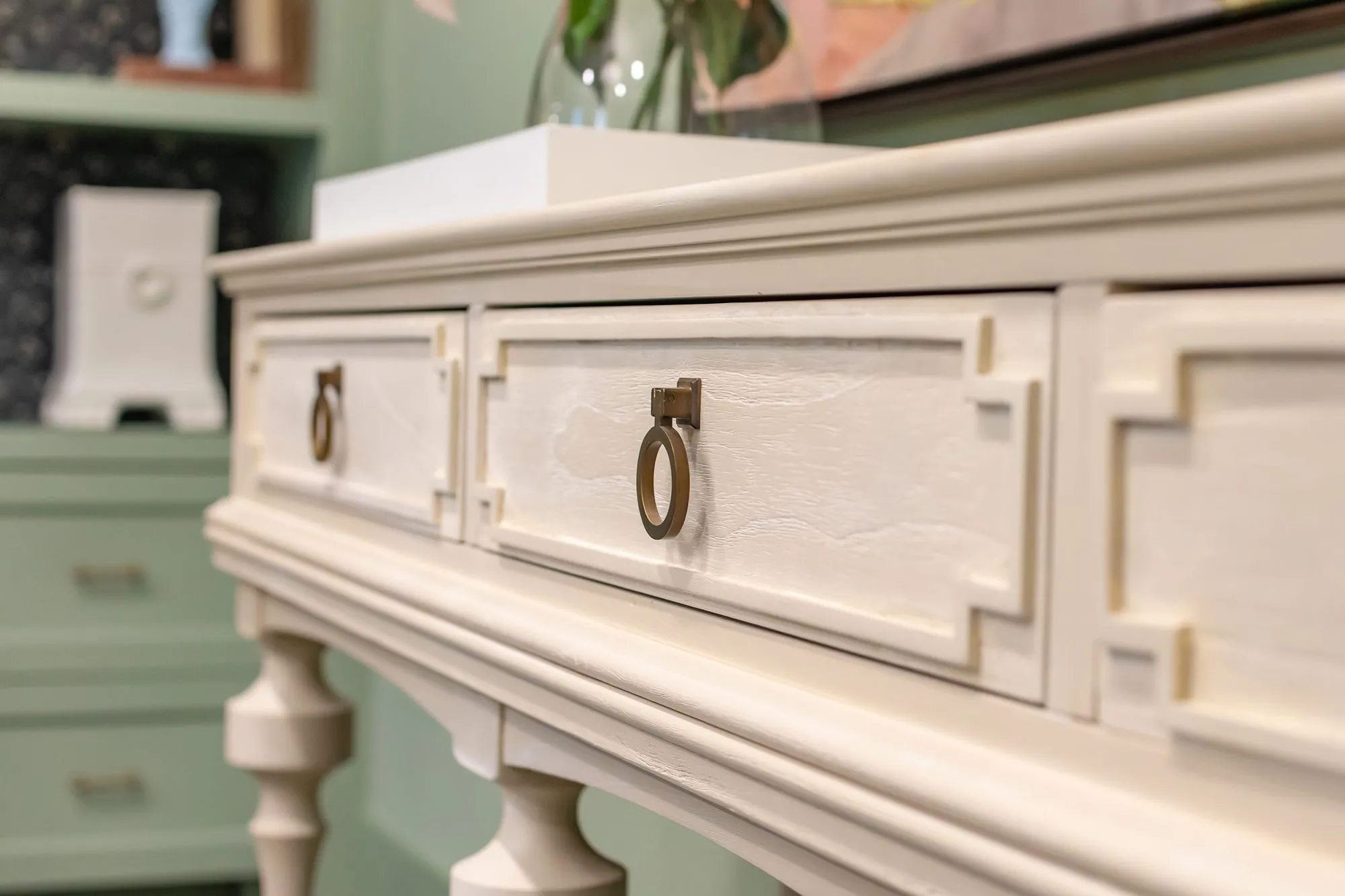 Senior living interior detail: cream painted console with ring pulls and turned legs, sage cabinets behind
