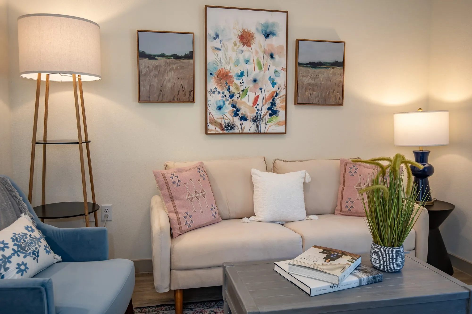 Senior living model living room loveseat with pink and white pillows below a floral painting and two landscapes