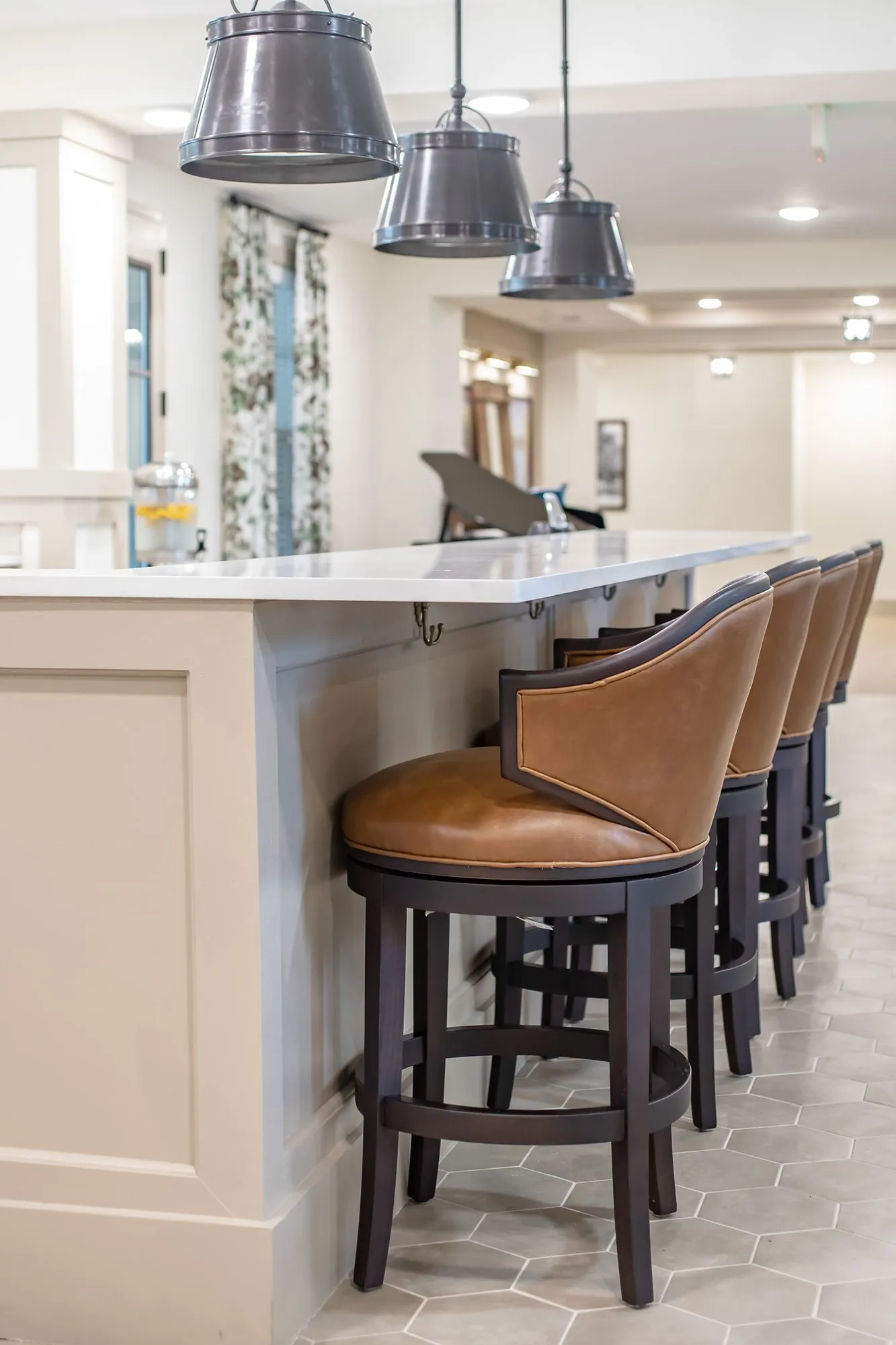 Senior living interior detail: white counter with cognac leather swivel barstools under grey metal pendants