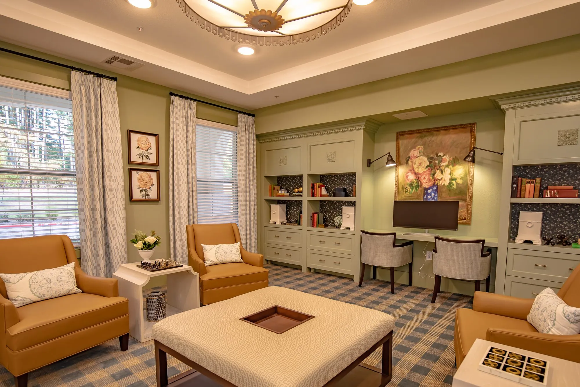 Senior living club room from the window side, camel leather chairs and an ottoman, sage built-ins with a floral painting