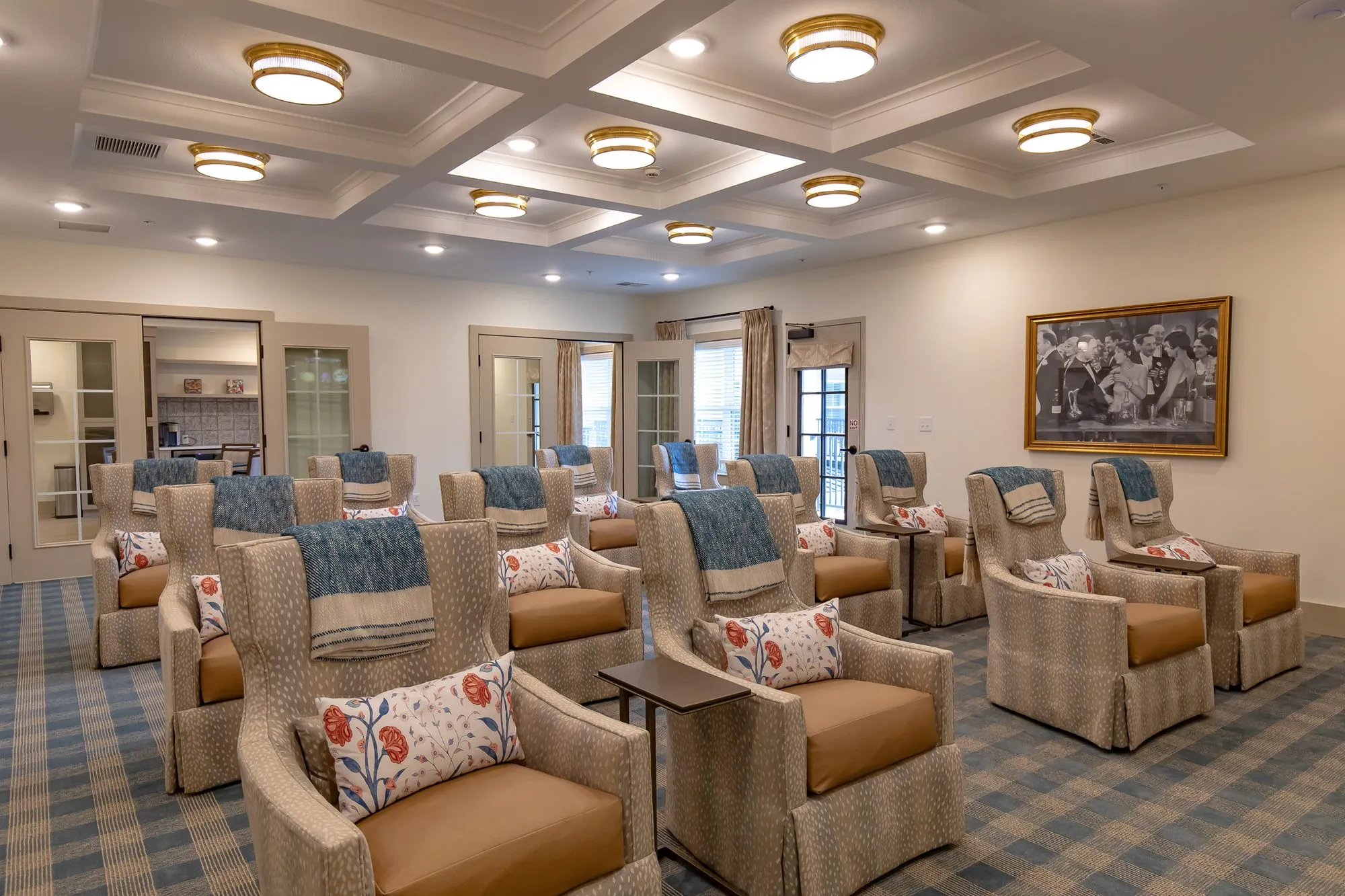 Senior living theatre room with rows of fawn print recliners under a coffered ceiling, glass doors along the back