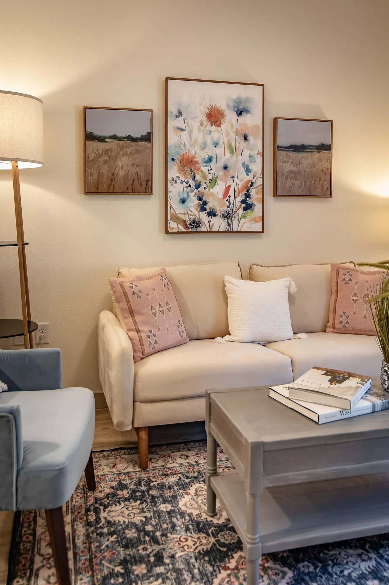 Senior living model living room with a cream loveseat, pink pillows and a grey coffee table on a blue rug