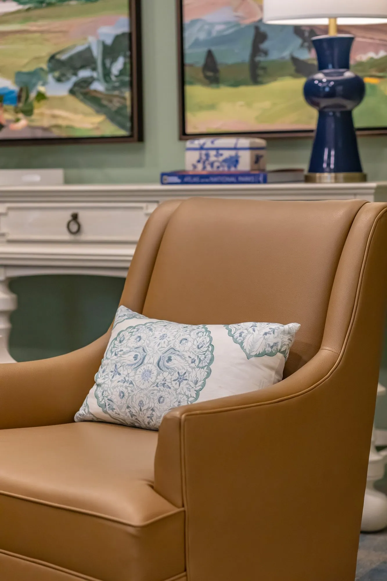 Senior living interior detail: camel leather armchair with a paisley pillow beside a white console with a navy lamp