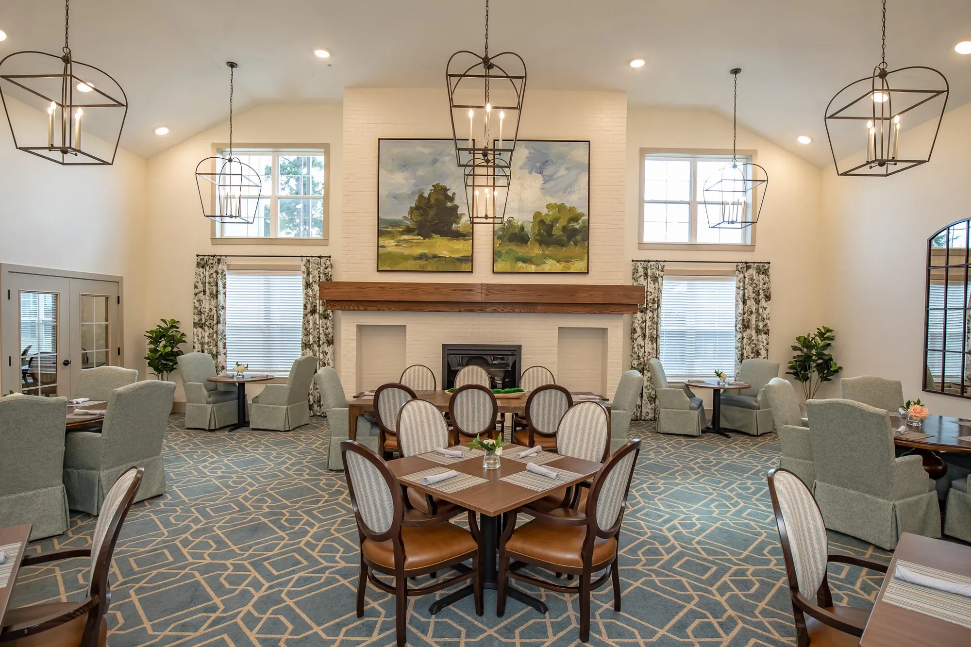 Senior living dining room facing the white brick fireplace, black lantern pendants and oval back chairs at square tables
