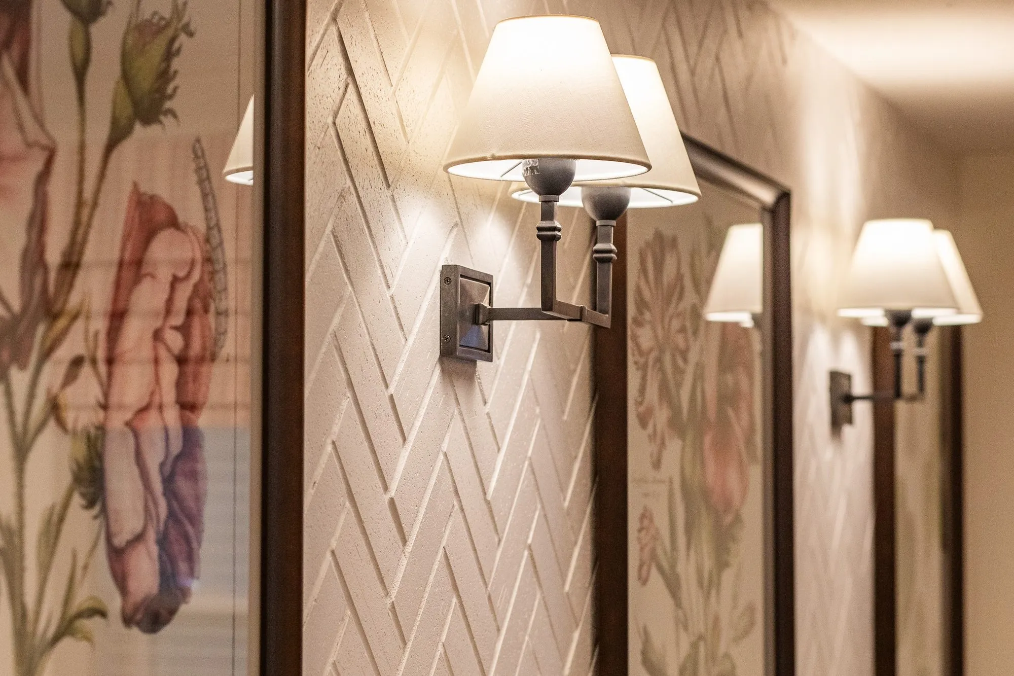 Senior living interior detail: white shaded wall sconces on a white herringbone textured wall beside floral prints