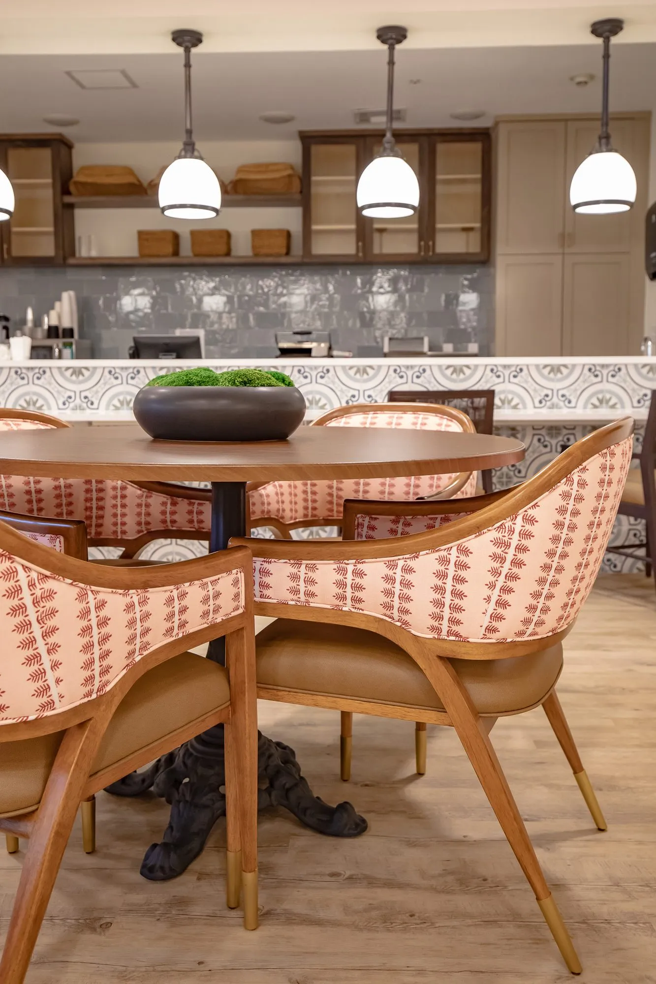 Senior living interior detail: coral striped bistro chairs with wood frames around a pedestal table, pendants above