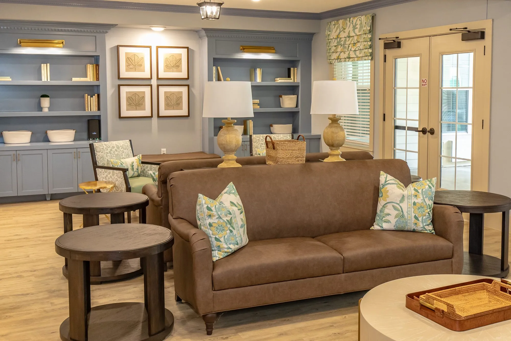 Senior living lounge with a brown leather sofa and patterned armchair before blue grey built-ins, French doors