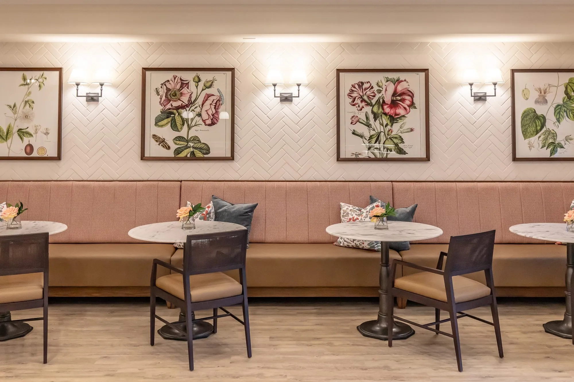 Senior living interior detail: pink banquette with marble bistro tables and black chairs below botanical prints and sconces