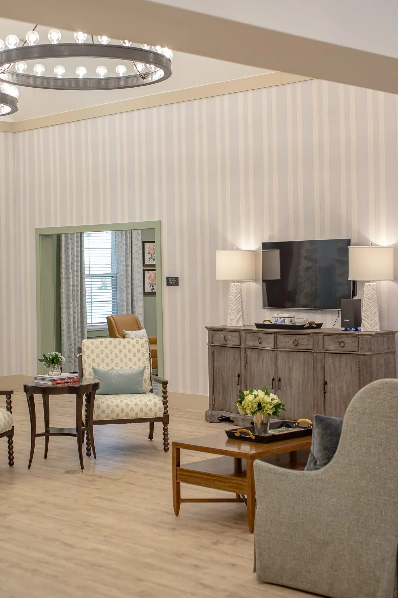 Senior living sitting area with a patterned armchair, wood coffee table and TV on a weathered sideboard by striped walls