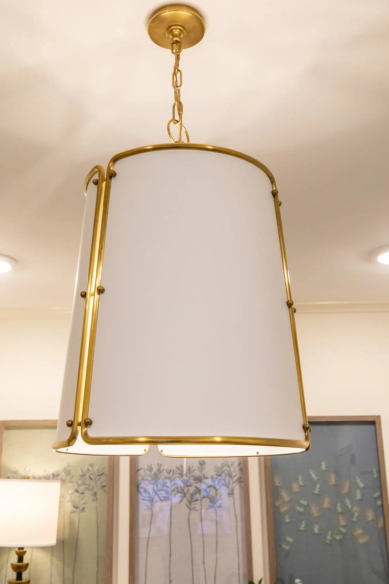 Senior living interior detail: looking up at a white drum pendant with a brass frame