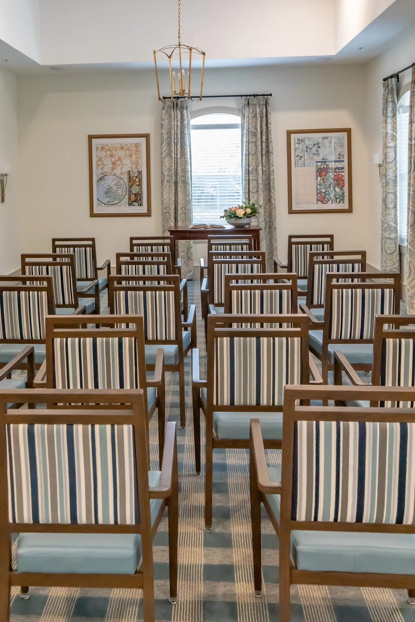 Senior living chapel from the aisle, rows of striped chairs facing a table under a brass lantern