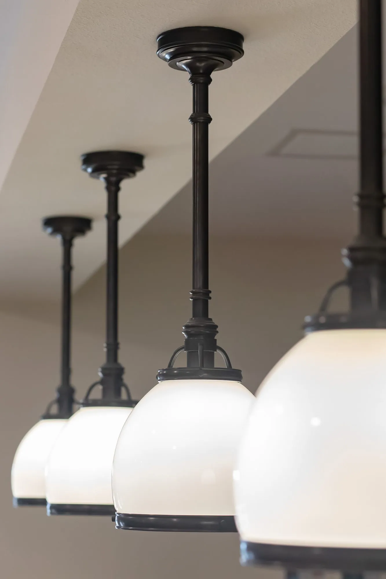 Senior living interior detail: row of black stem pendants with white opal glass shades receding along a soffit