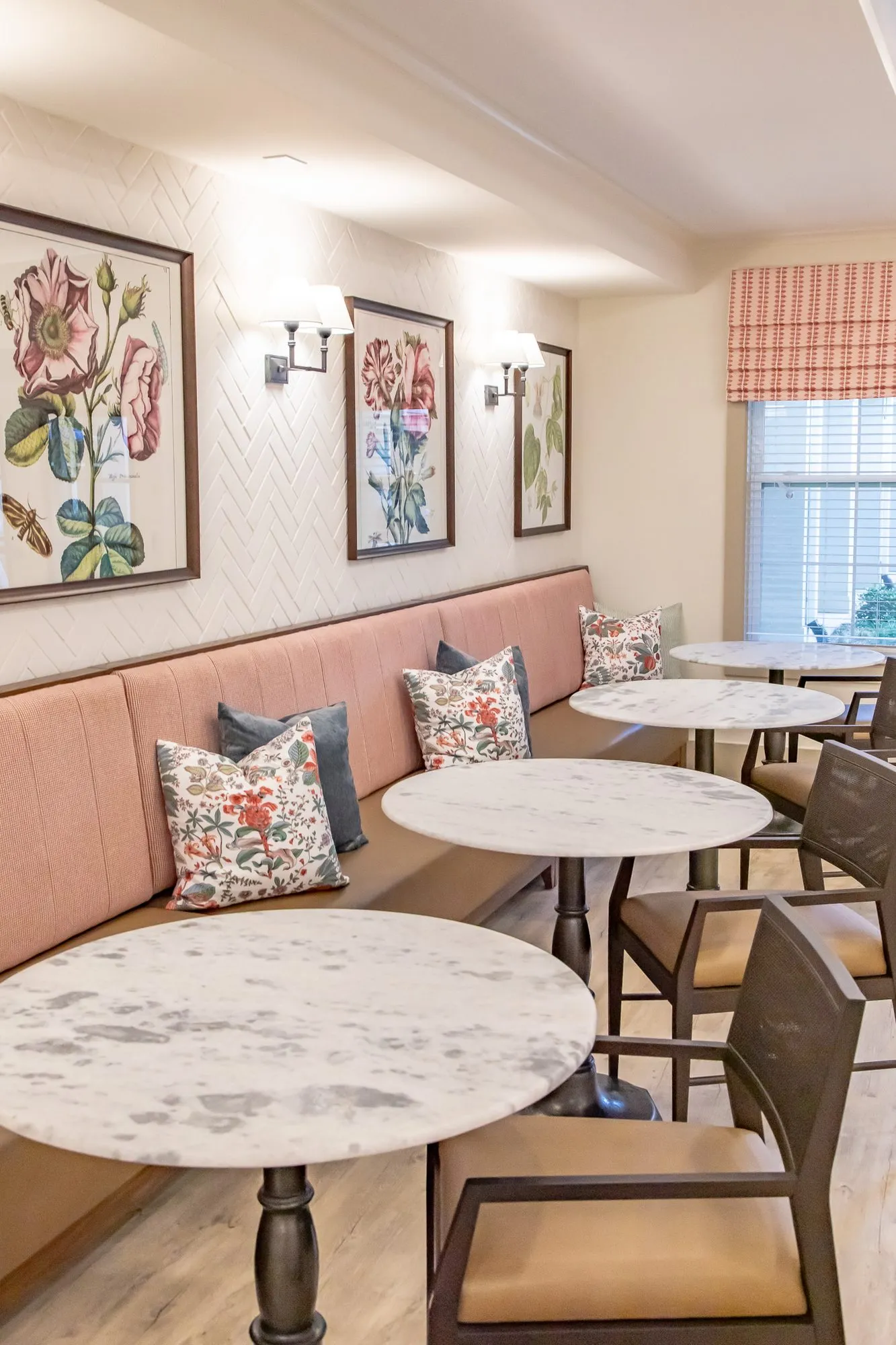 Senior living interior detail: pink banquette with marble bistro tables, floral pillows and botanical prints