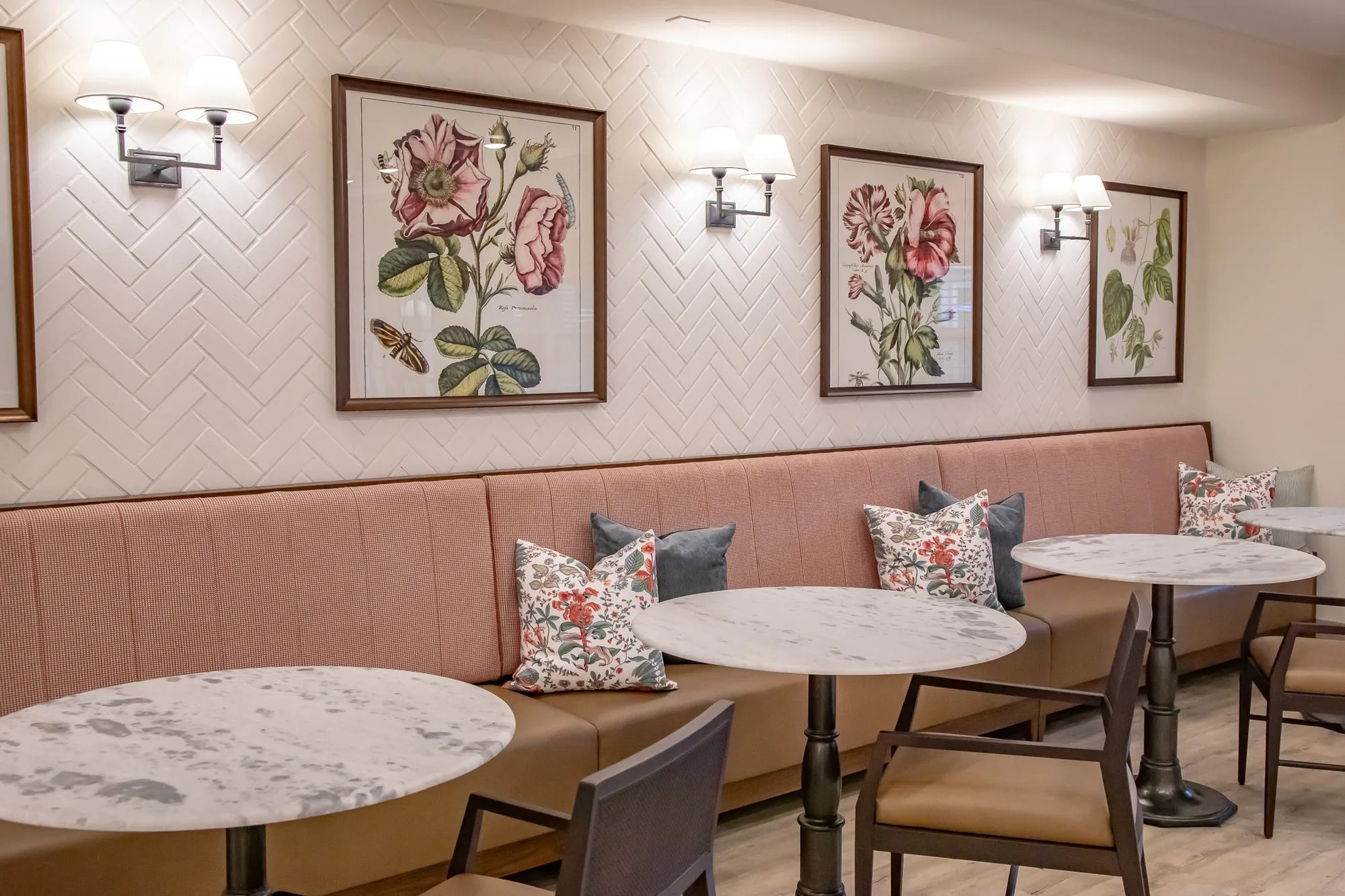 Senior living interior detail: pink banquette with floral and grey pillows, marble bistro tables, herringbone tile