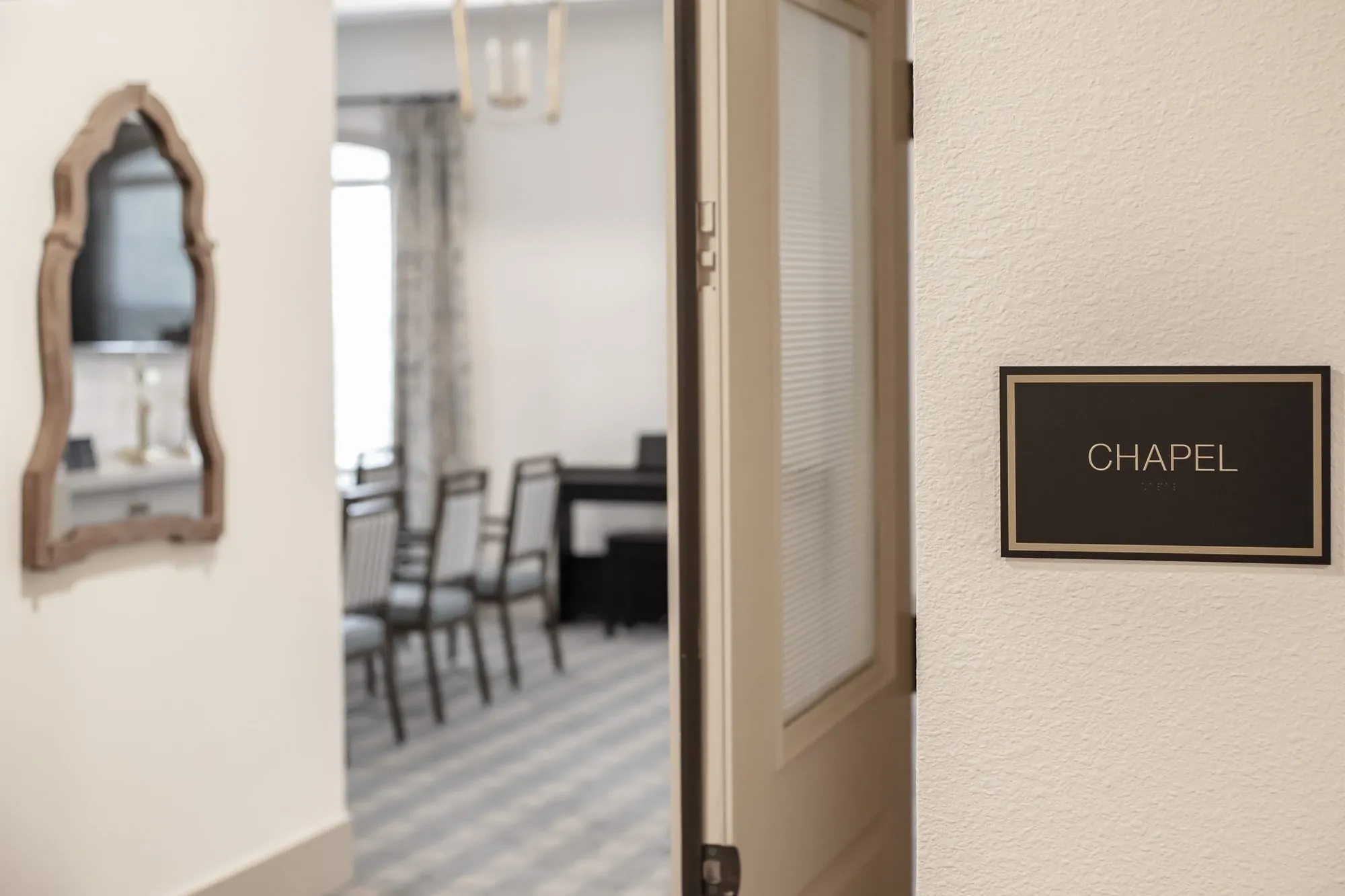 Senior living chapel doorway with a Chapel sign beside a carved wood mirror, rows of chairs inside