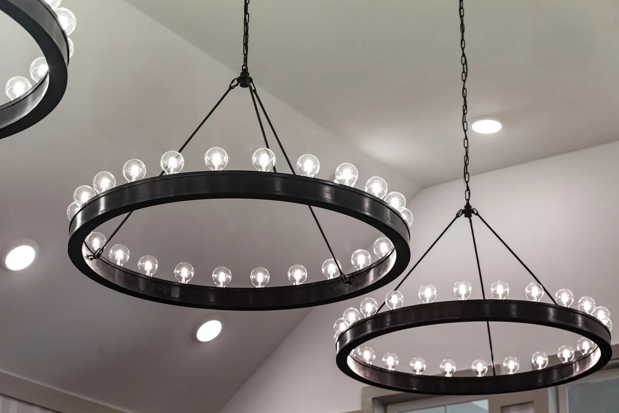 Senior living interior detail: two black iron ring chandeliers with globe bulbs under a sloped white ceiling