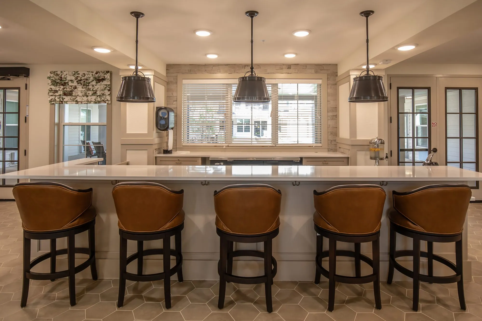 Senior living kitchen with five cognac leather swivel barstools at the island on hexagon tile under three metal pendants