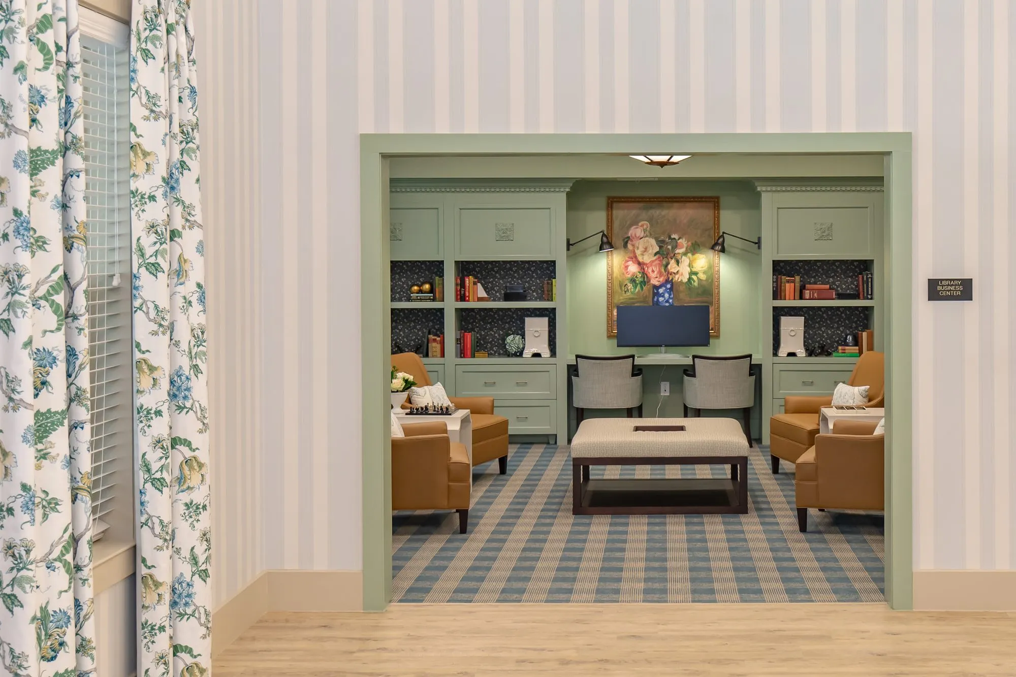 Senior living club room with camel chairs and built-ins seen through a doorway, a floral curtain and striped wallcovering