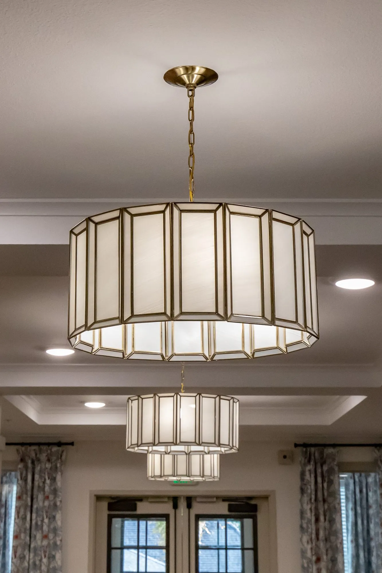 Senior living interior detail: looking up at a white and brass faceted drum pendant, another behind, above French doors