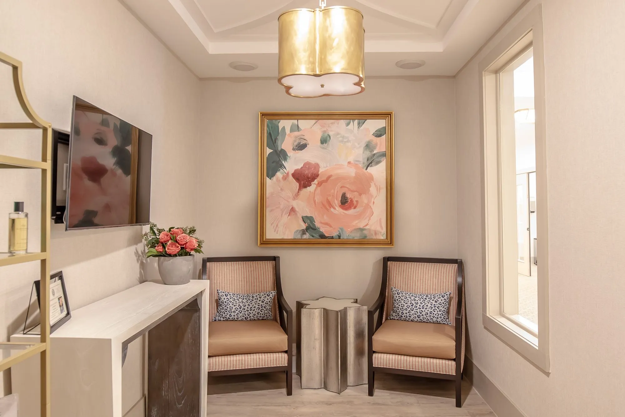 Senior living small sitting room with two striped armchairs below a floral painting, a TV and console opposite