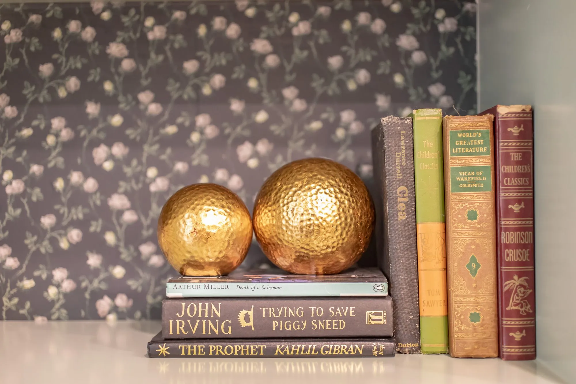 Senior living interior detail: gold hammered spheres and vintage books on a shelf against dark rose wallpaper