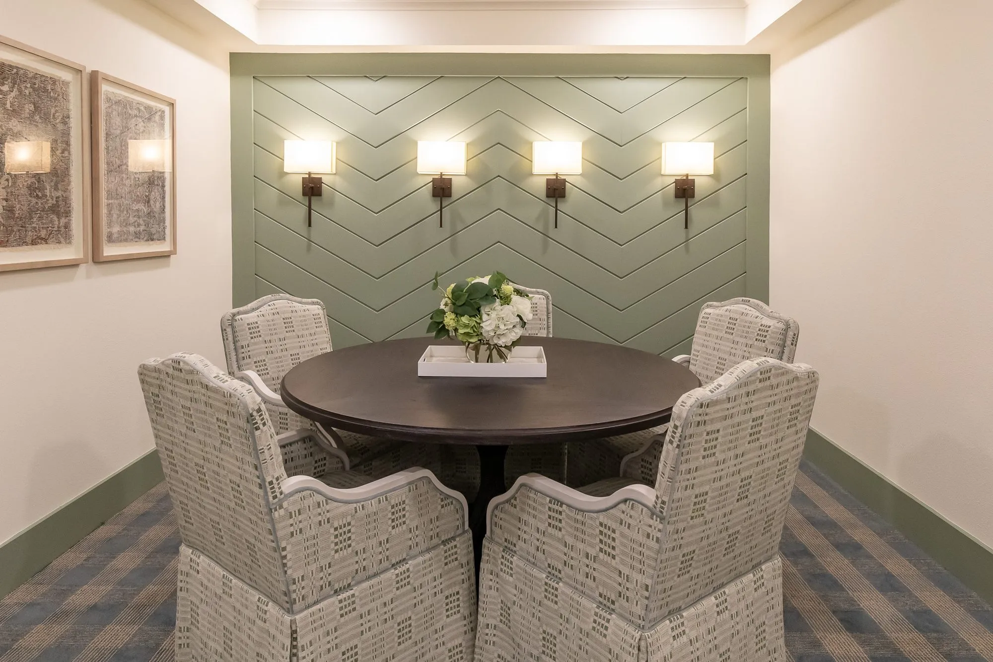 Senior living private dining nook with skirted chairs around a round table by a sage chevron panelled wall with sconces