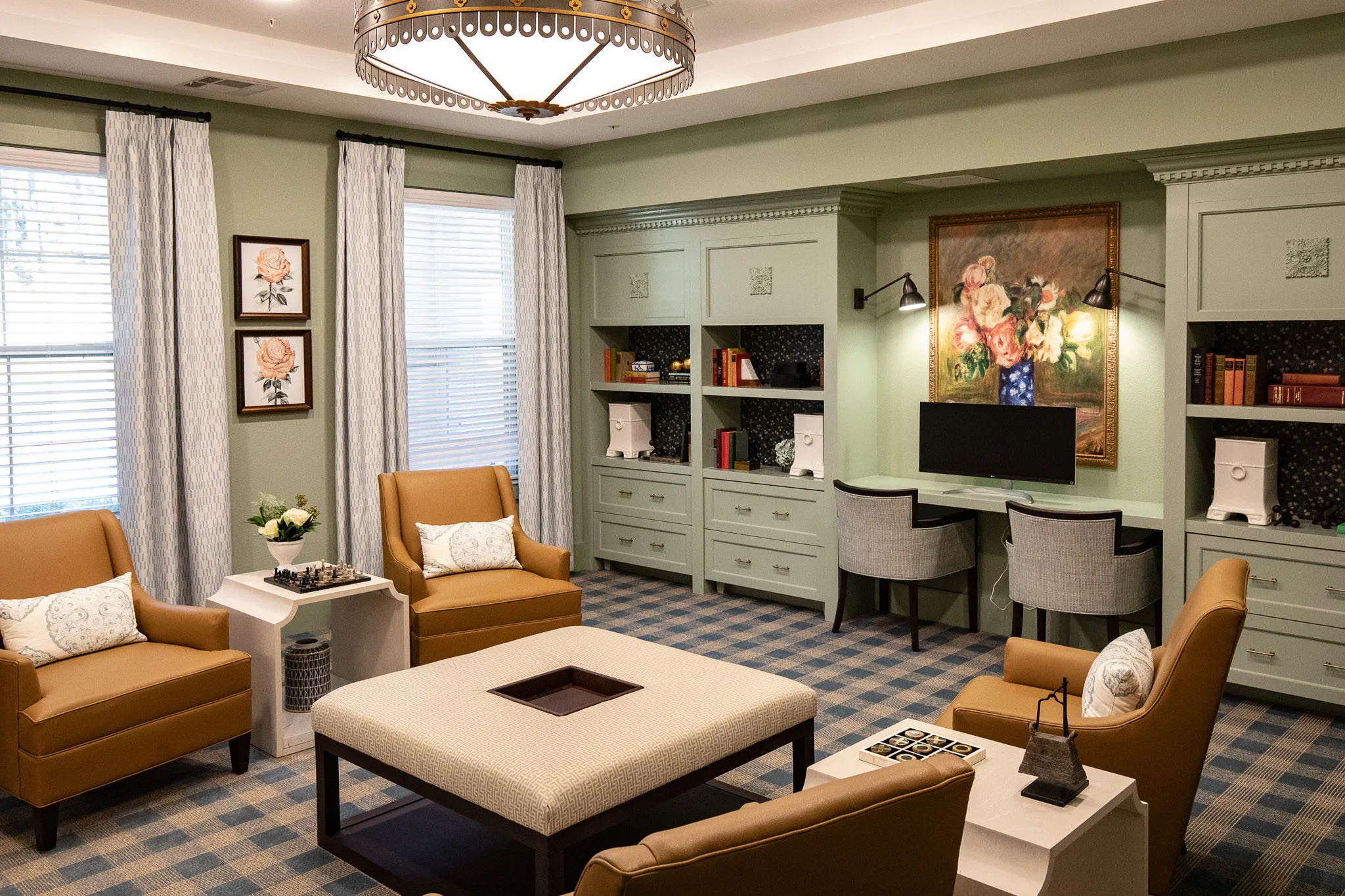 Senior living club room with camel leather chairs and a linen ottoman between sage built-ins and a floral still life