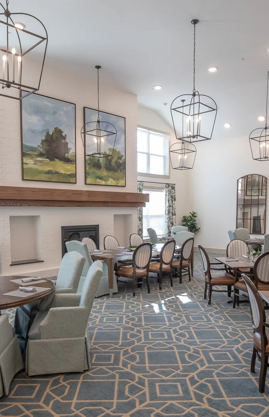 Senior living dining room with a white brick fireplace and sage skirted chairs, interior design by Banko Design at The Blake At Tyler, Tyler, Texas