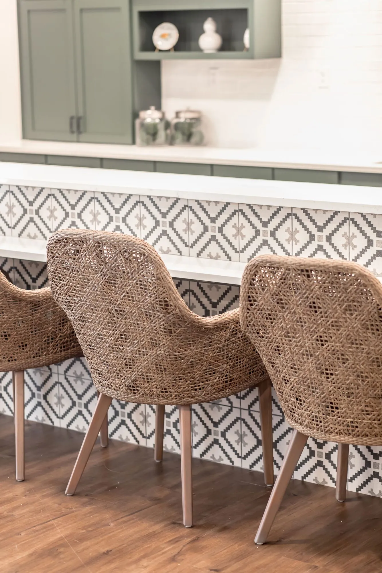 Senior living bistro with woven counter chairs at a bar fronted with black and white geometric tile, sage cabinets above
